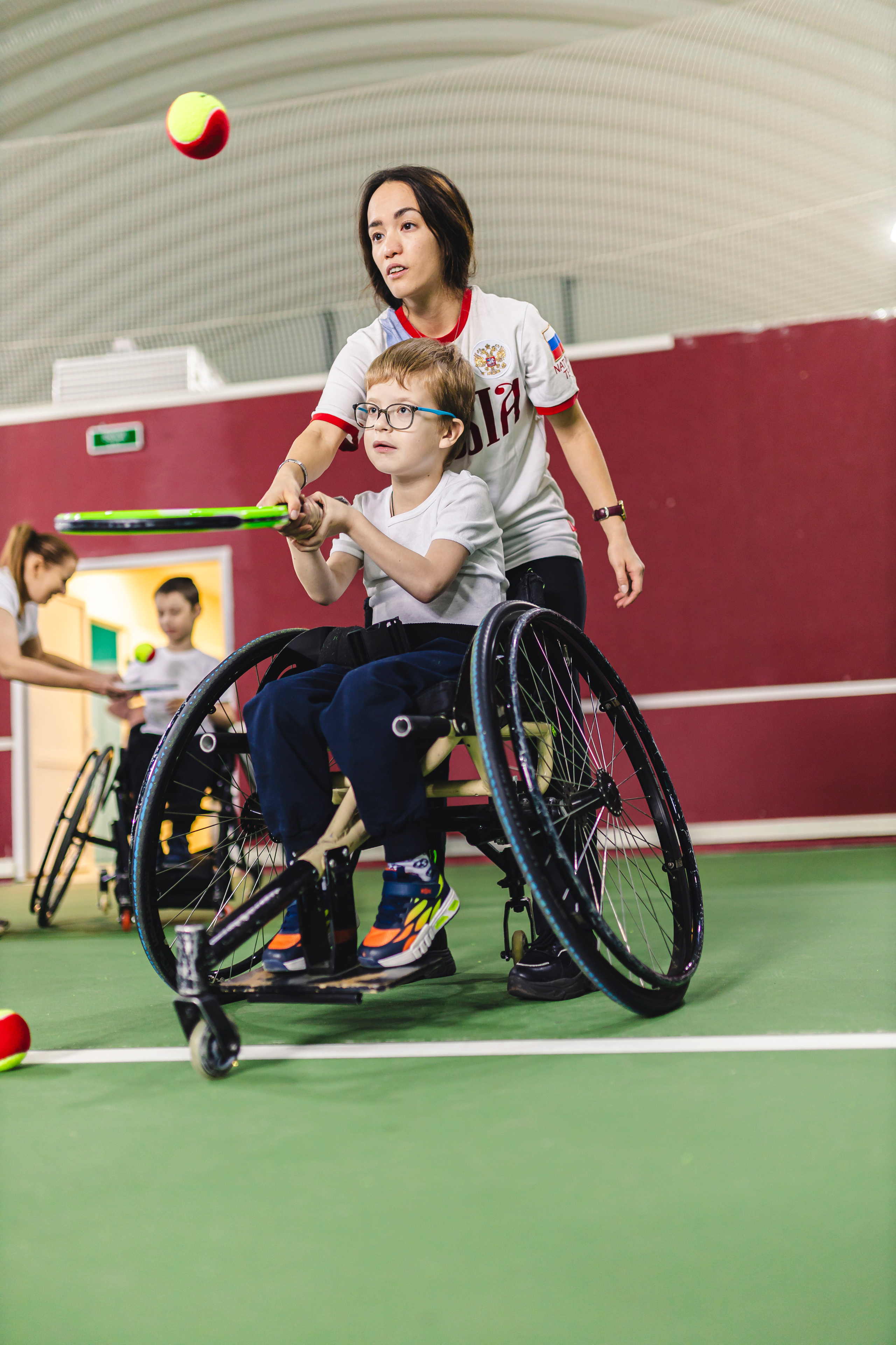тренер отбивает с мальчиком мячик теннисной ракеткой 