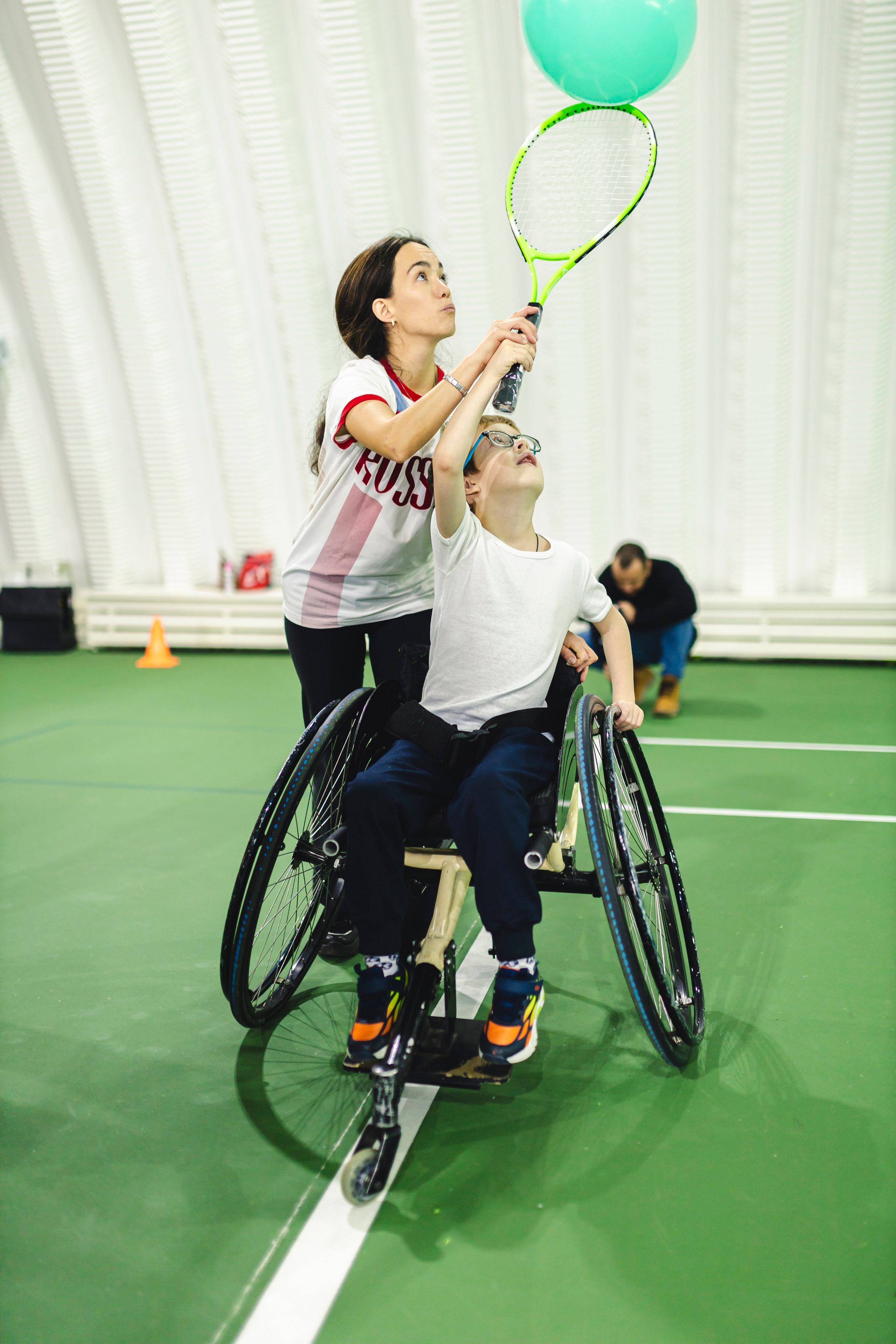 мальчик на коляске теннисной ракеткой отбивает воздушный шарик 