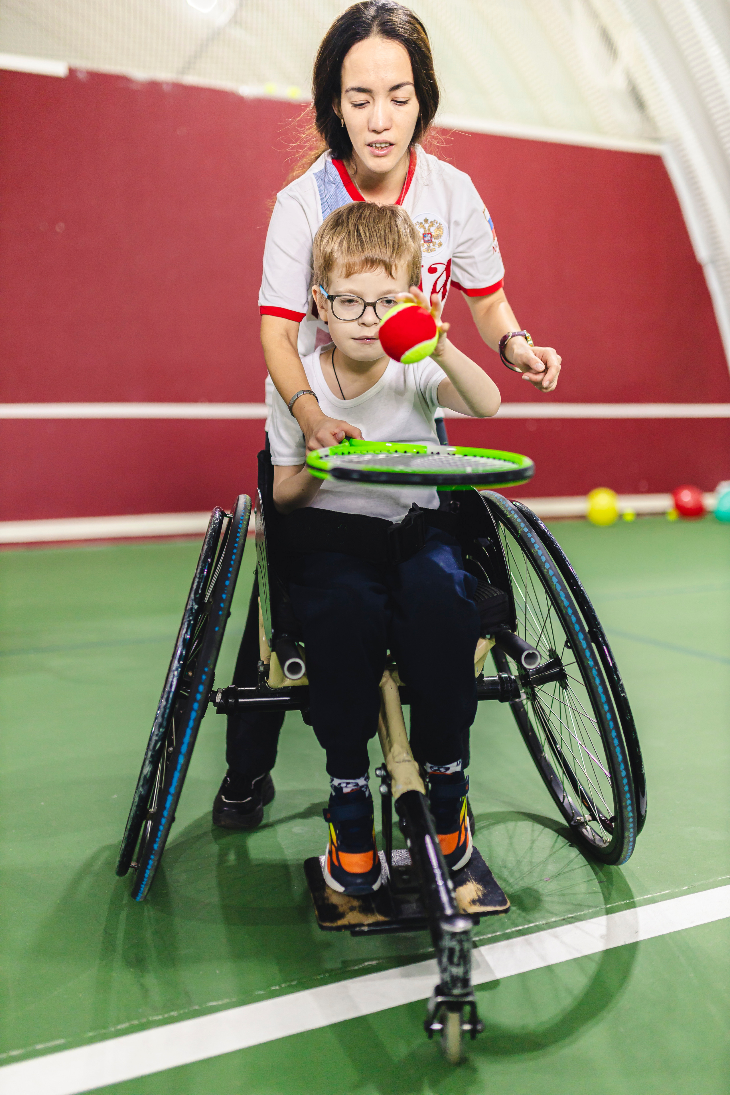 девушка помогает юному теннисисту играть с ракеткой 