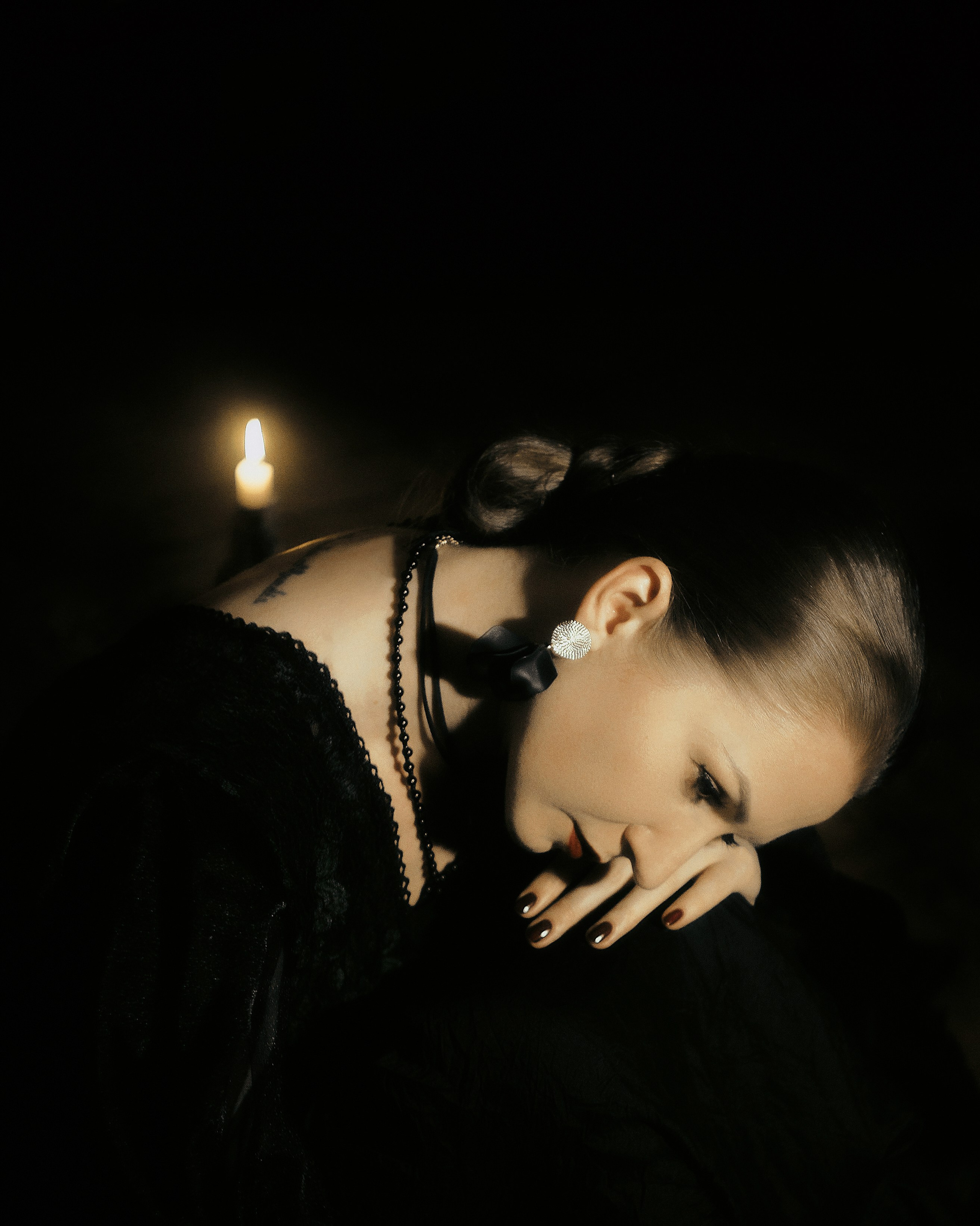 студийная фотосессия нуар, женский портрет с опущенным взглядом и свечой, чёрные украшения, фотограф Москва