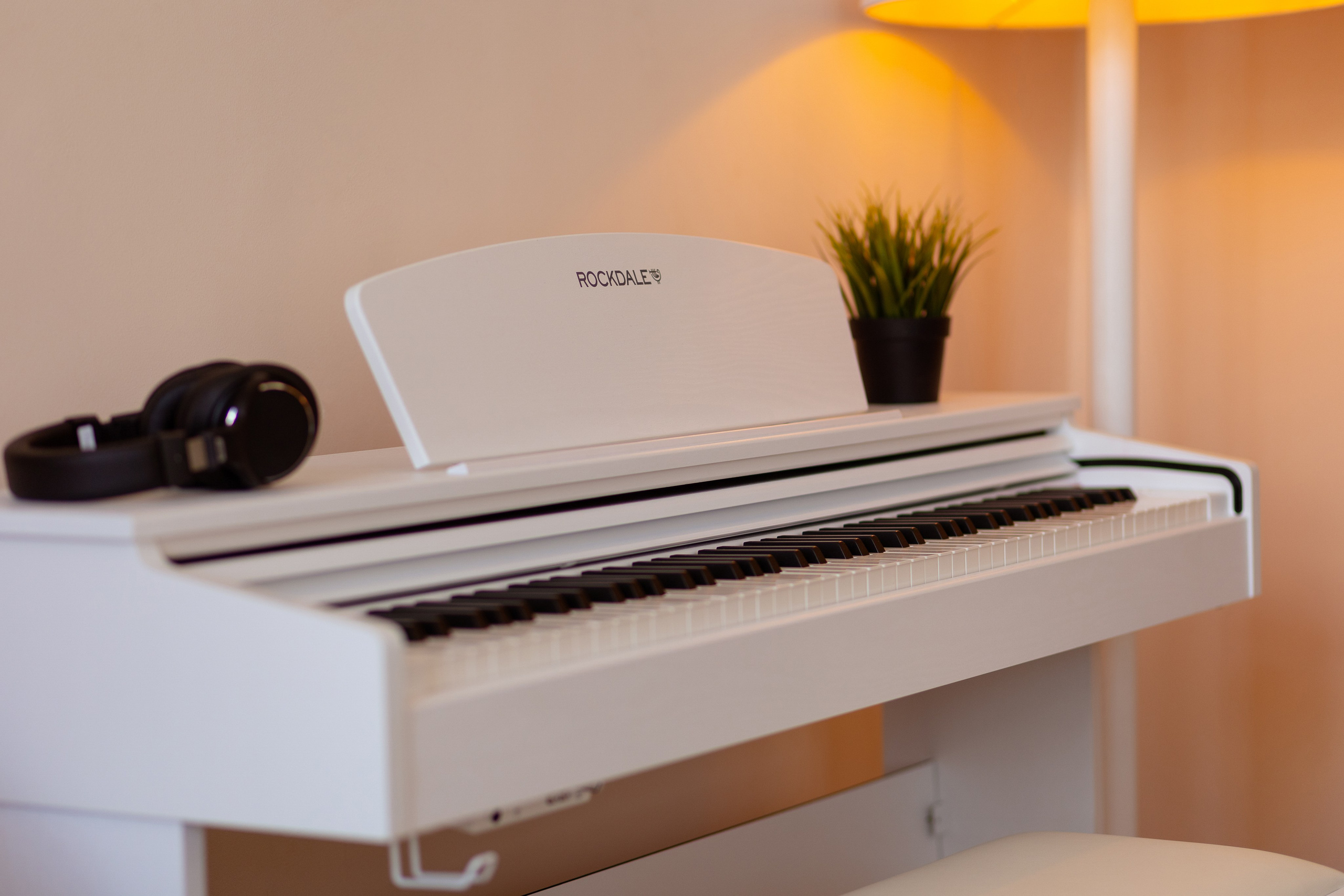 На белом пианино лежат наушники и стоит ваза.