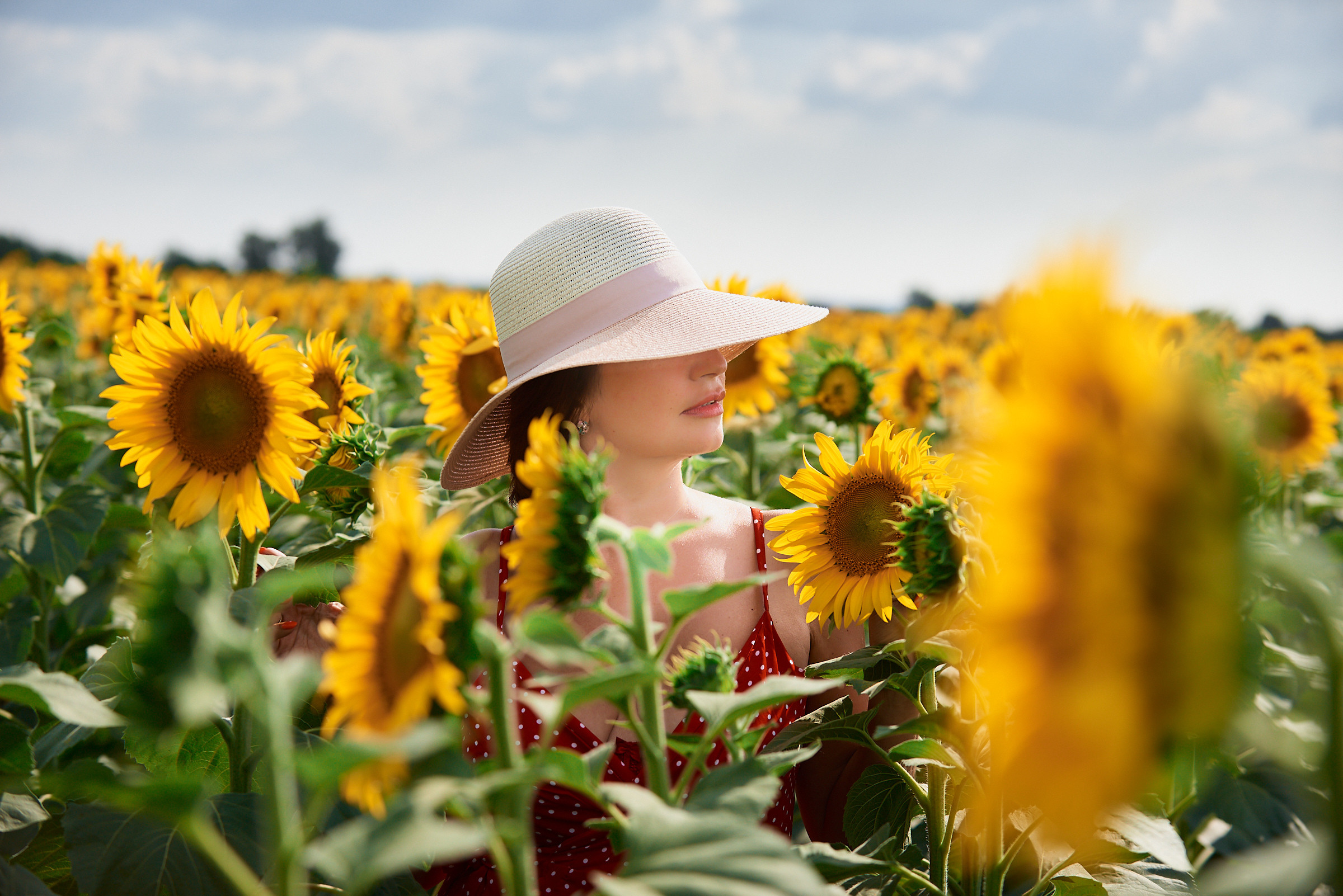 Стильная девушка в соломенной шляпе на поле с подсолнухами