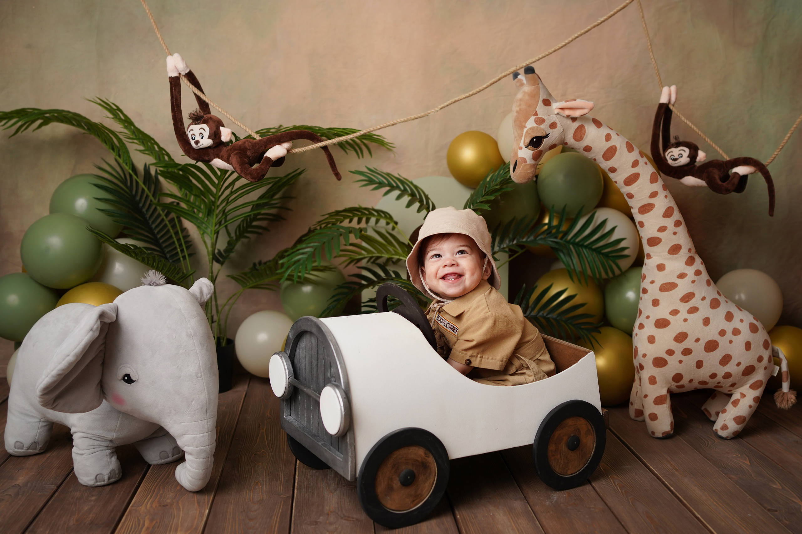 На фото фотосессия Первый годик в стиле сафари. Малыш сидит в машинке, рядом жираф, слон.