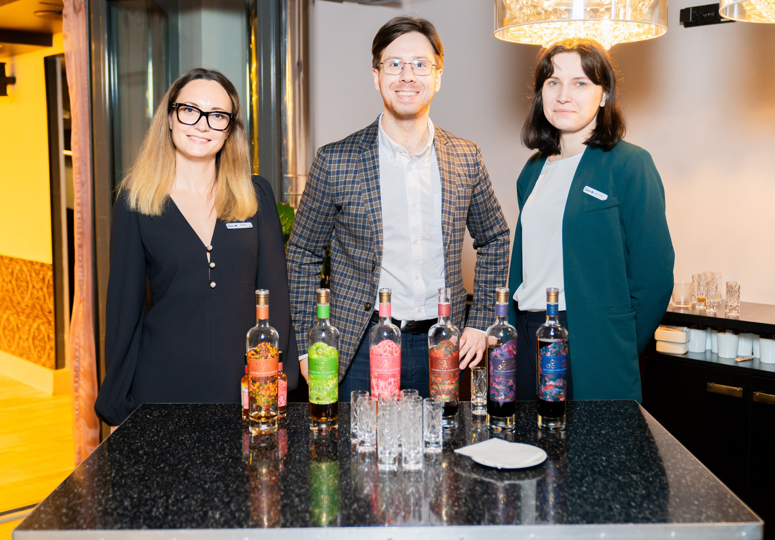 Три человека за барной стойкой с бутылками фирменных настоек на мероприятии в Radisson Sonya. Фото Евгения Мальцева (evrednix.ru).
