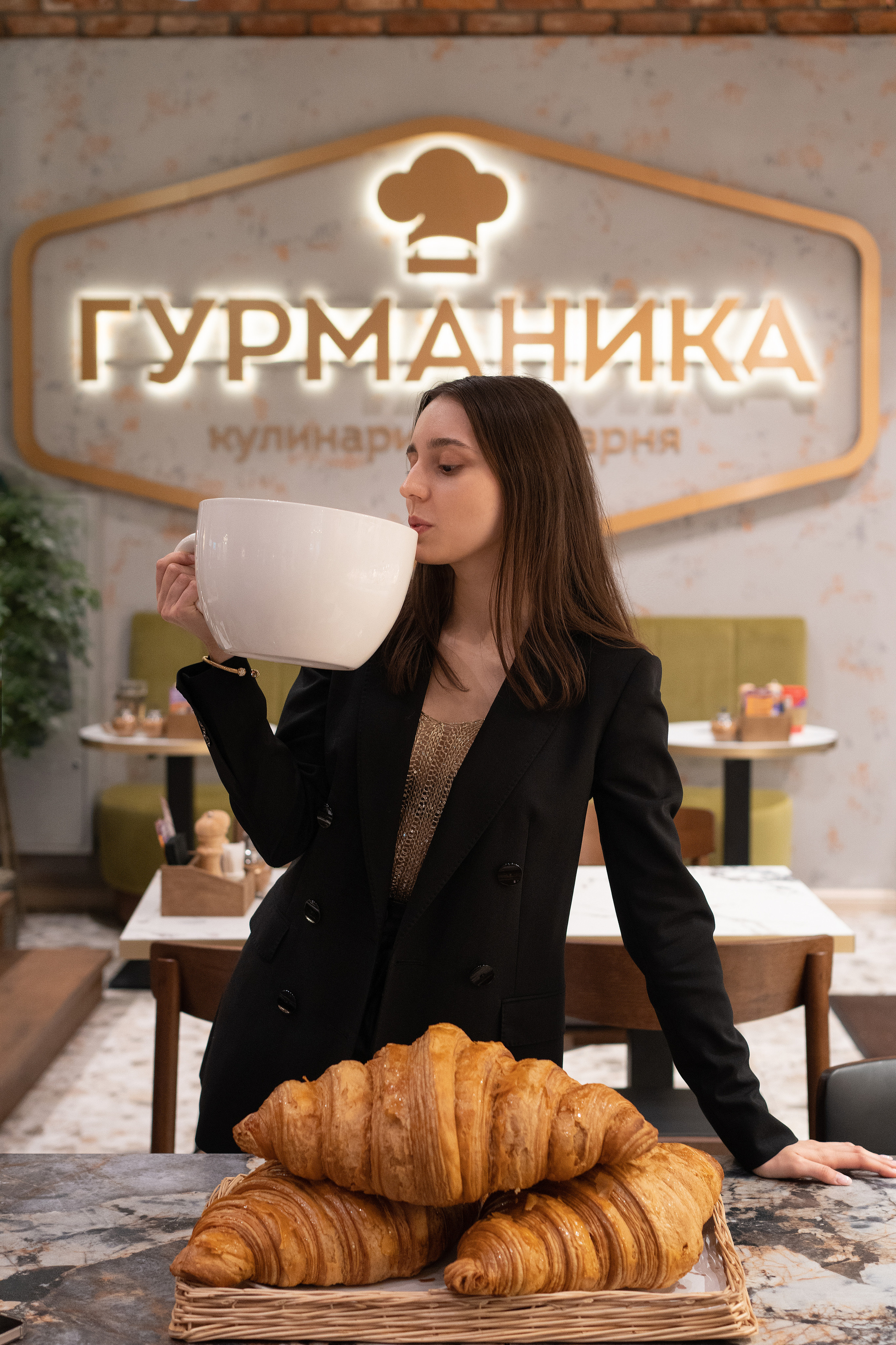 Девушка держит огромную кружку капучино и большой круассан. Промо акция в кафе Гурманика.  