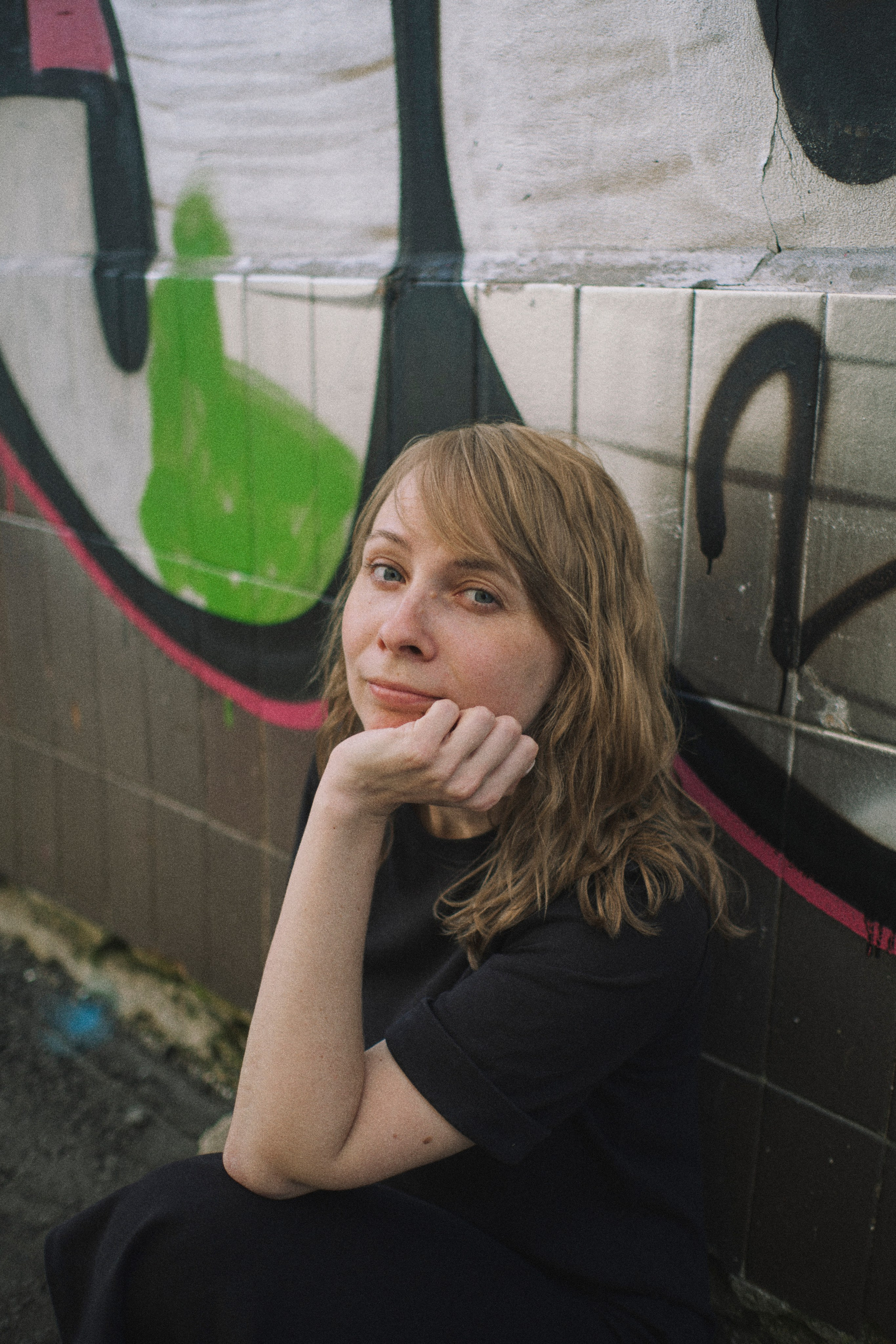 Женщина сидит у стены, подперев лицо рукой