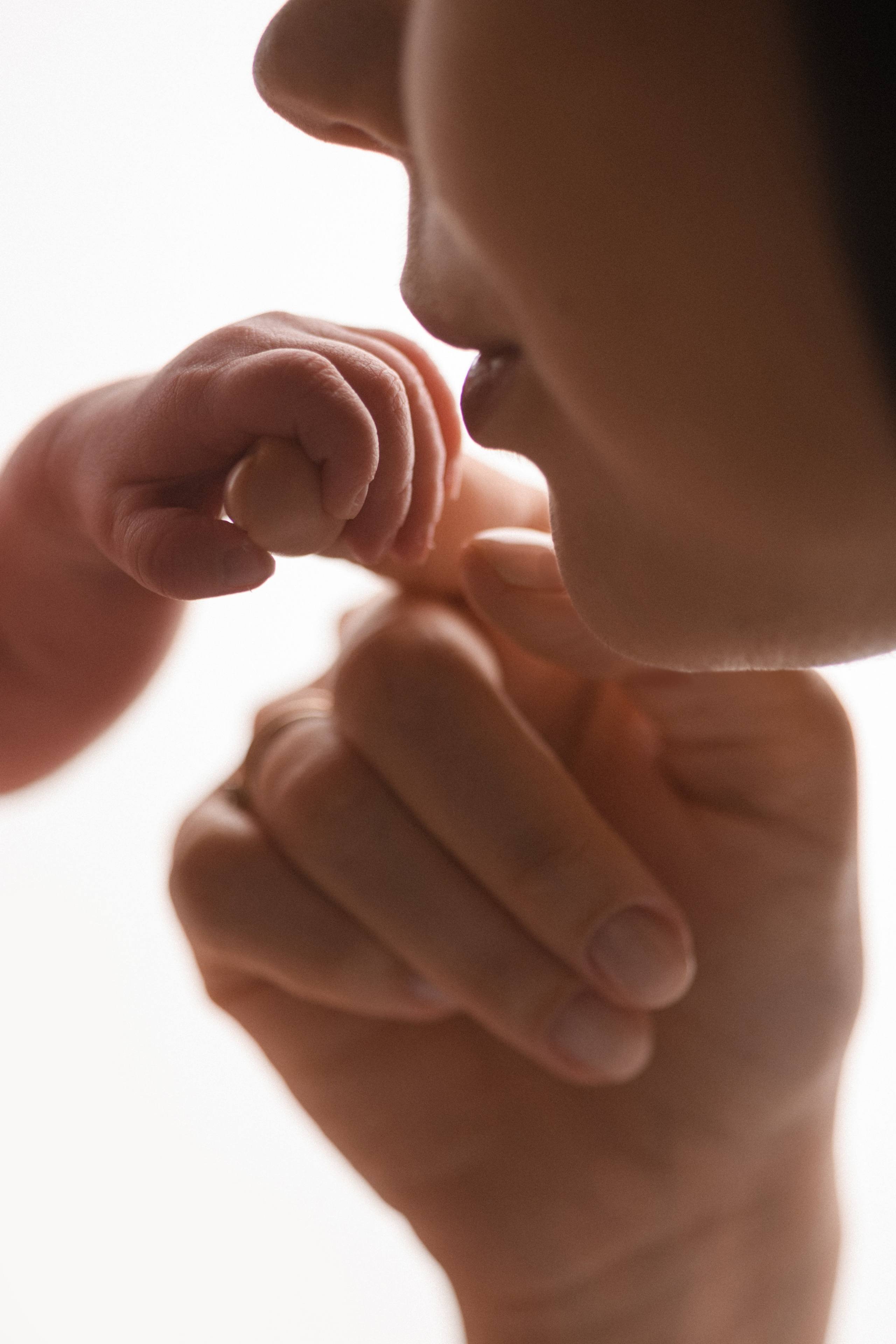 Мама целует ручку новорожденного малыша на белом фоне в фотостудии новорожденных Алёны Лариной в Липецке