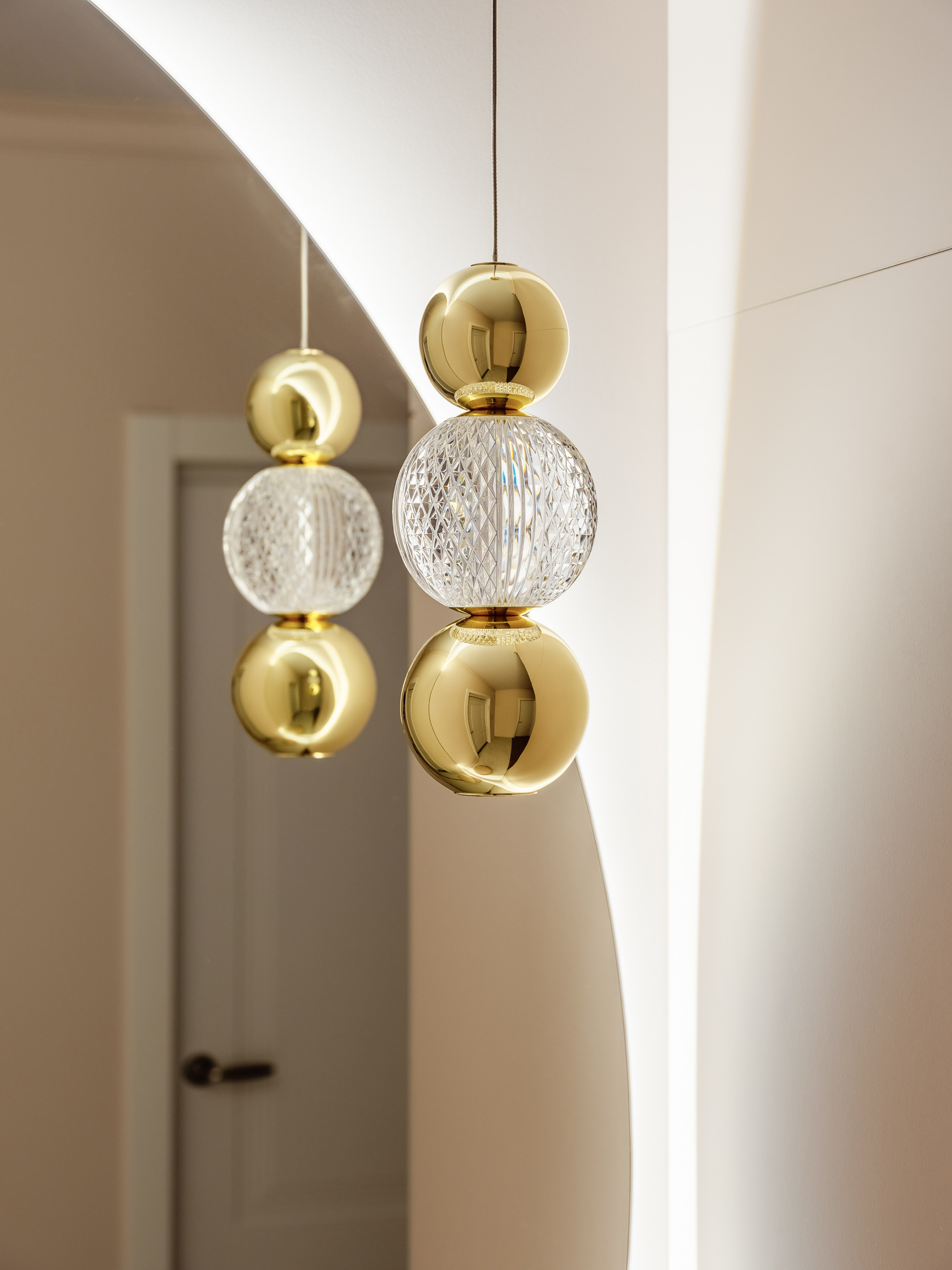 Элегантный подвесной светильник с золотыми элементами и хрустальной сферой отражается в зеркале, создавая акцент в современном интерьере прихожей. Дизайн Наталья Бунеева, стилист Наталья Якушева, фотограф Сергей Денисенко.