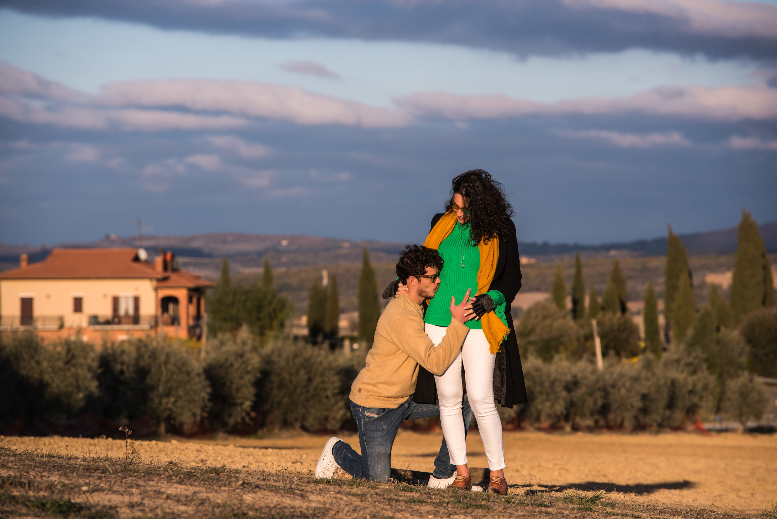 Мужчина обнимает беременную женщину в солнечном поле, пейзаж Тосканы, снято ранним утром.