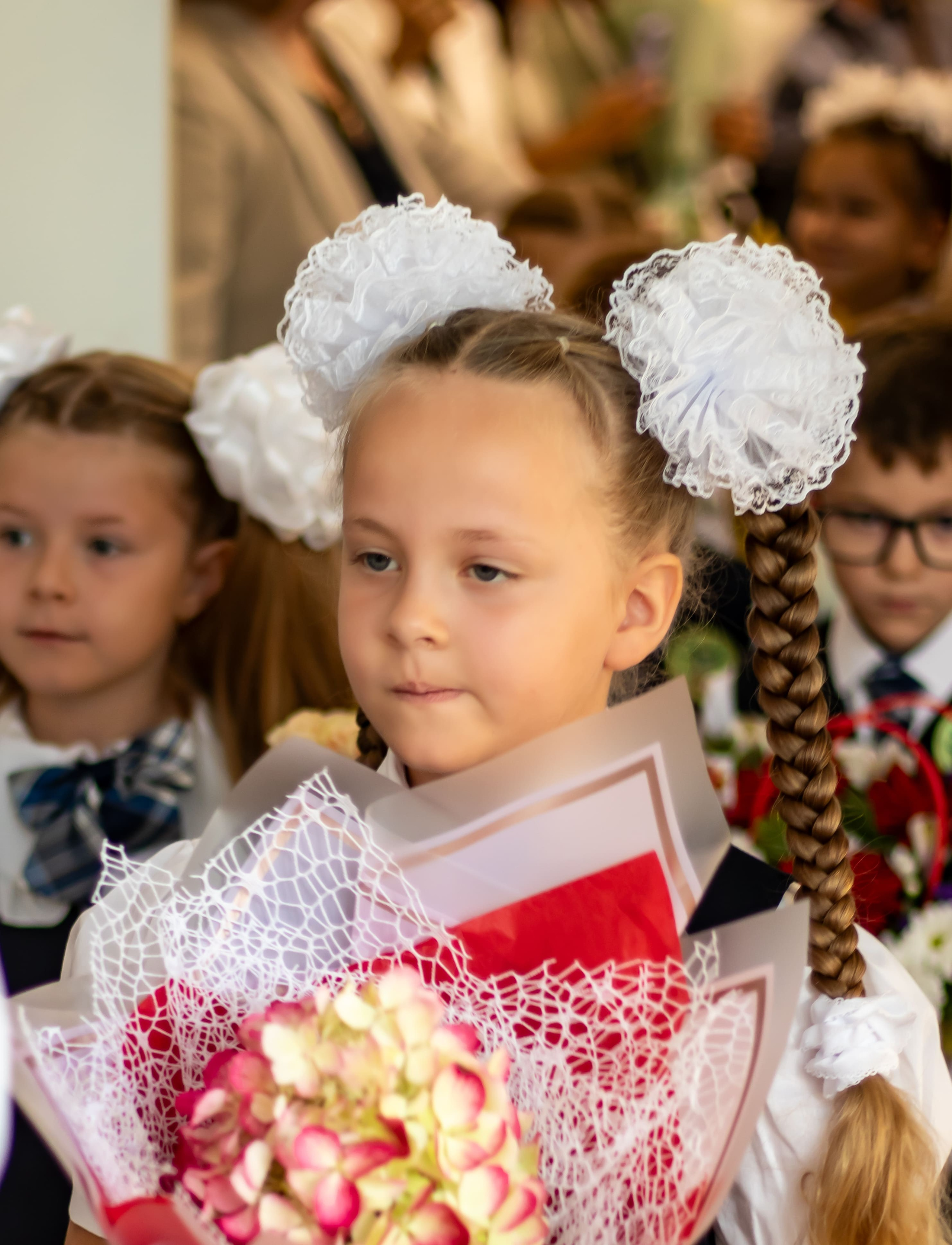 Первоклассница с белыми бантами и цветами на 1 сентября