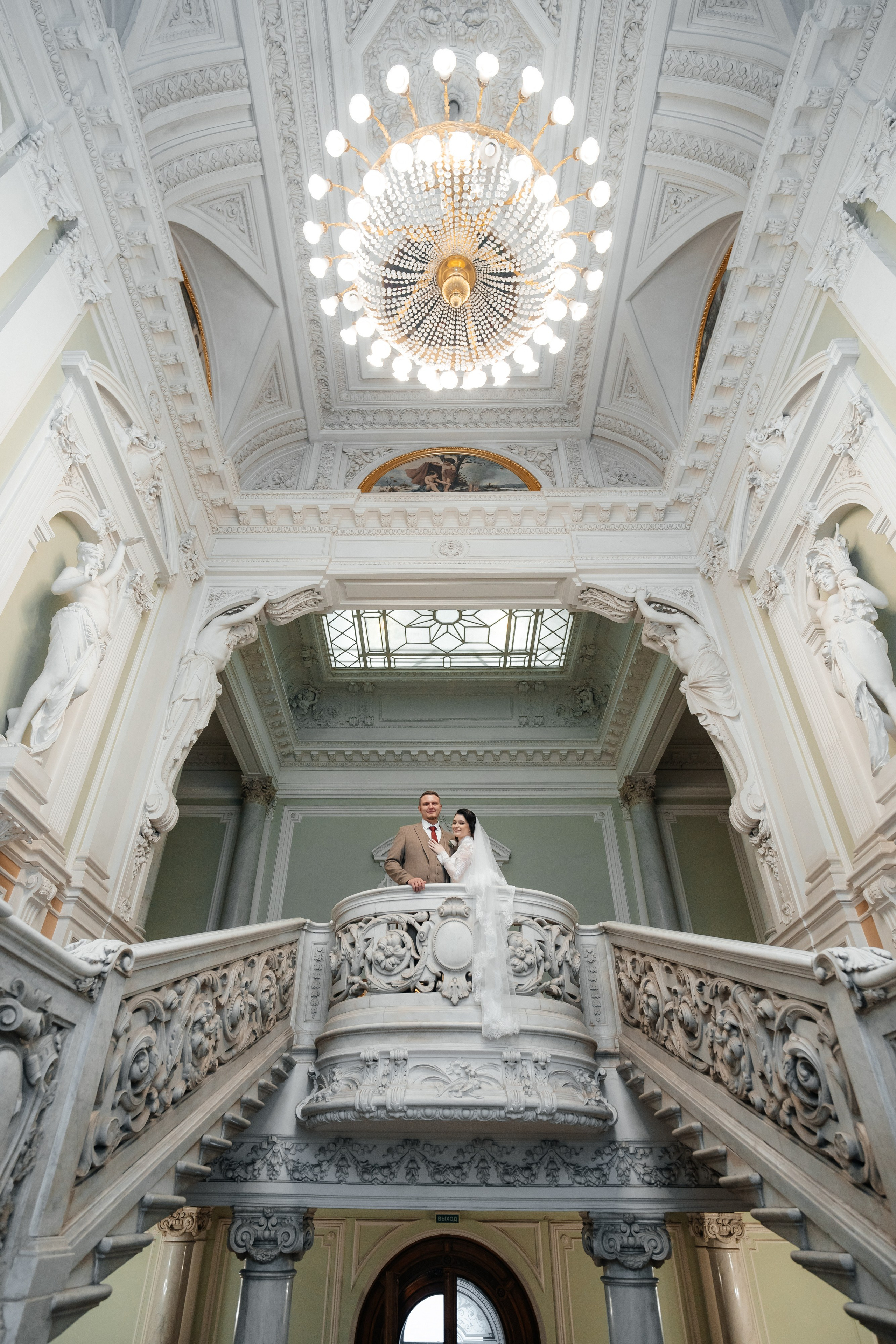 Свадебная фотосессия во Дворце Бракосочетания №1 Жених и невеста стоят на балконе фото с люстрой.
