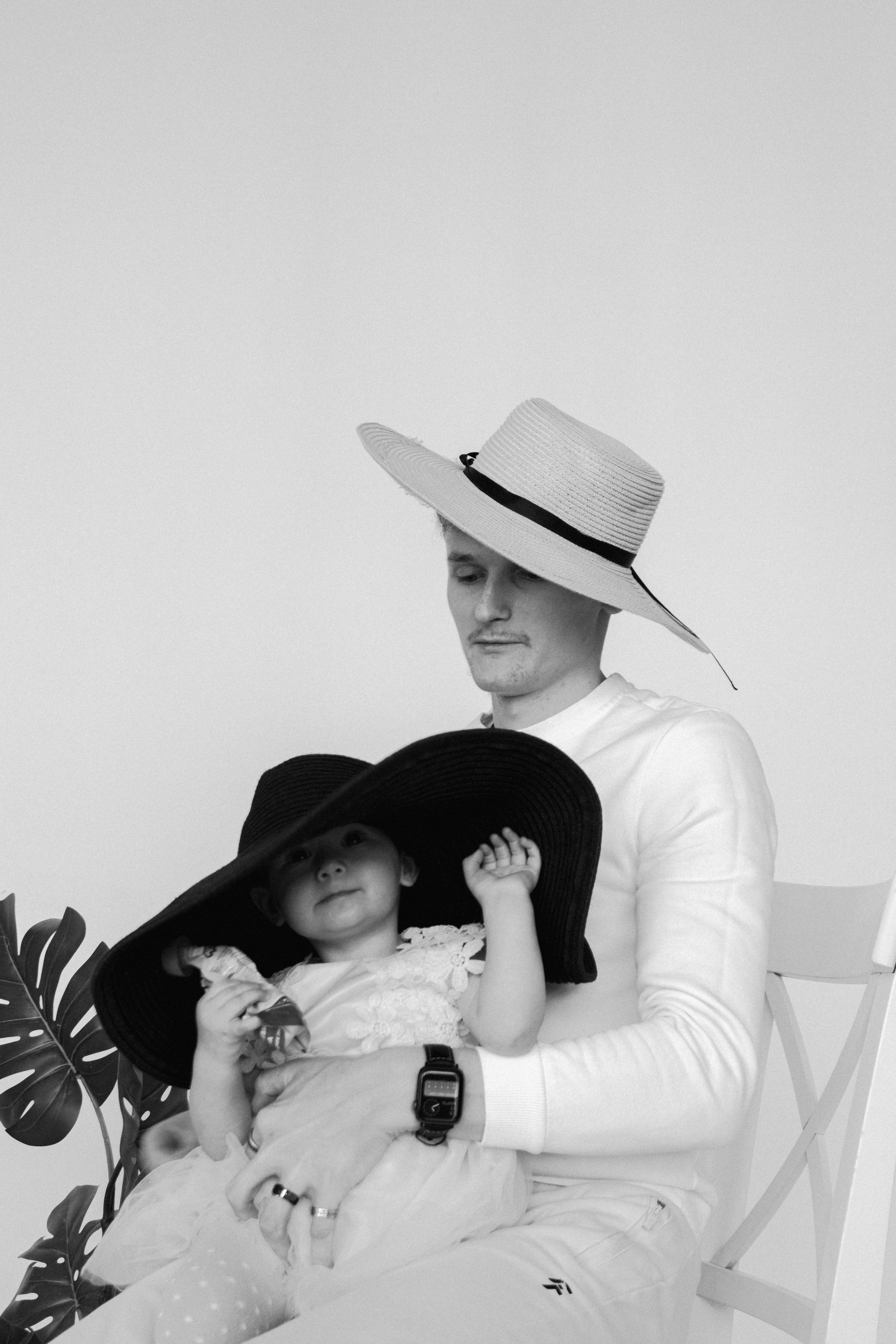 Папа с дочкой позируют в шляпах на фоне белой стены