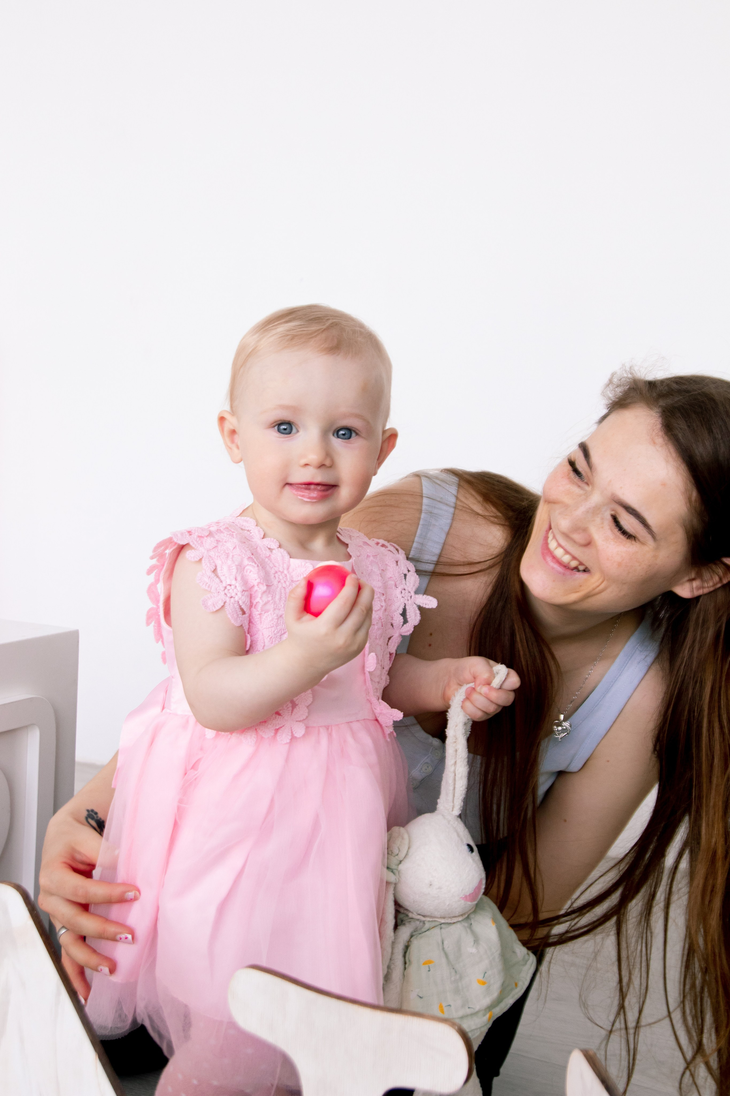 мама смотрит на дочку в розовом платье которая держит игрушку и украшение со своего именинного торта