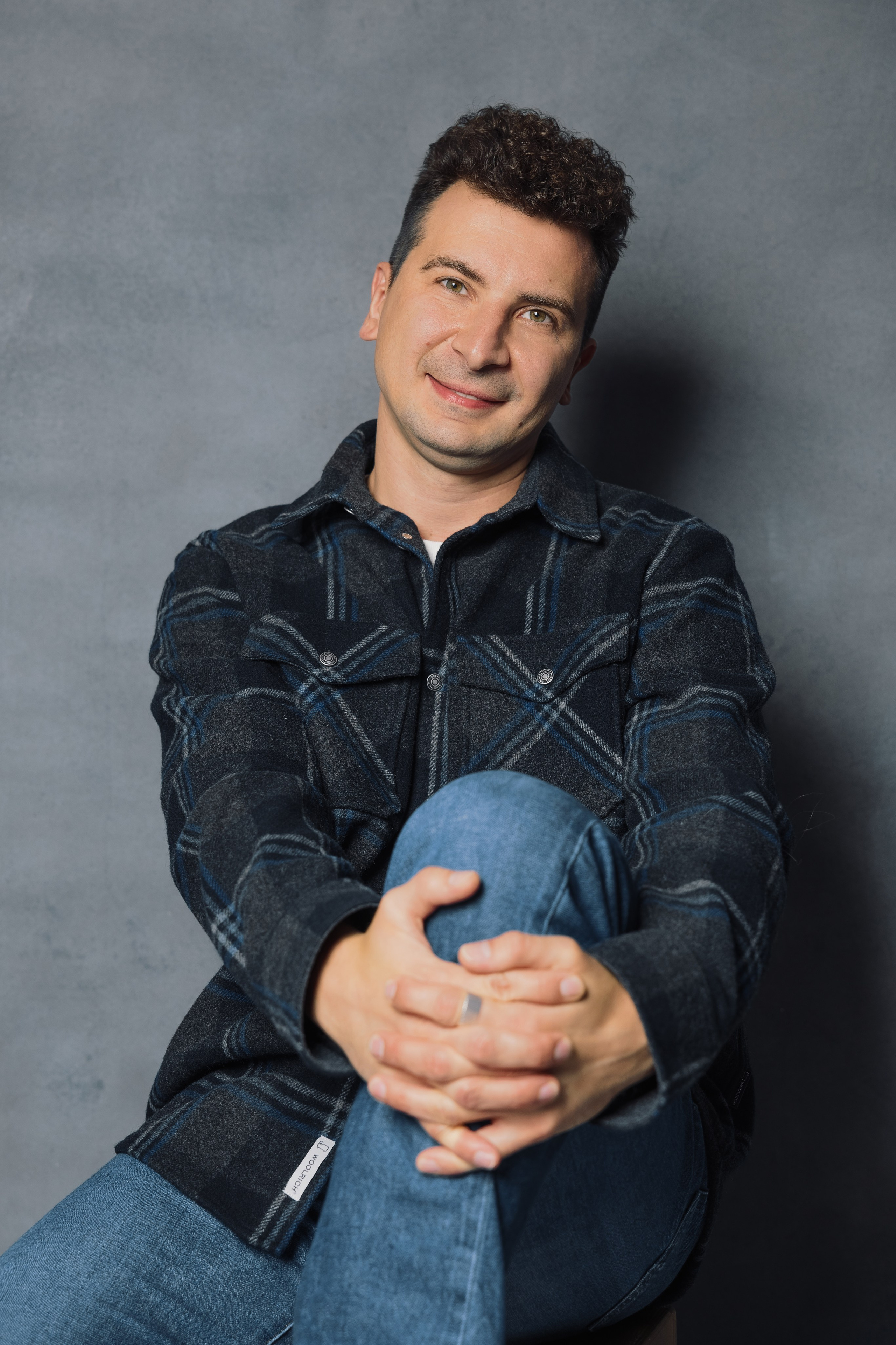 Портретная фотография мужчины в джинсах и клетчатой рубашке на сером фоне