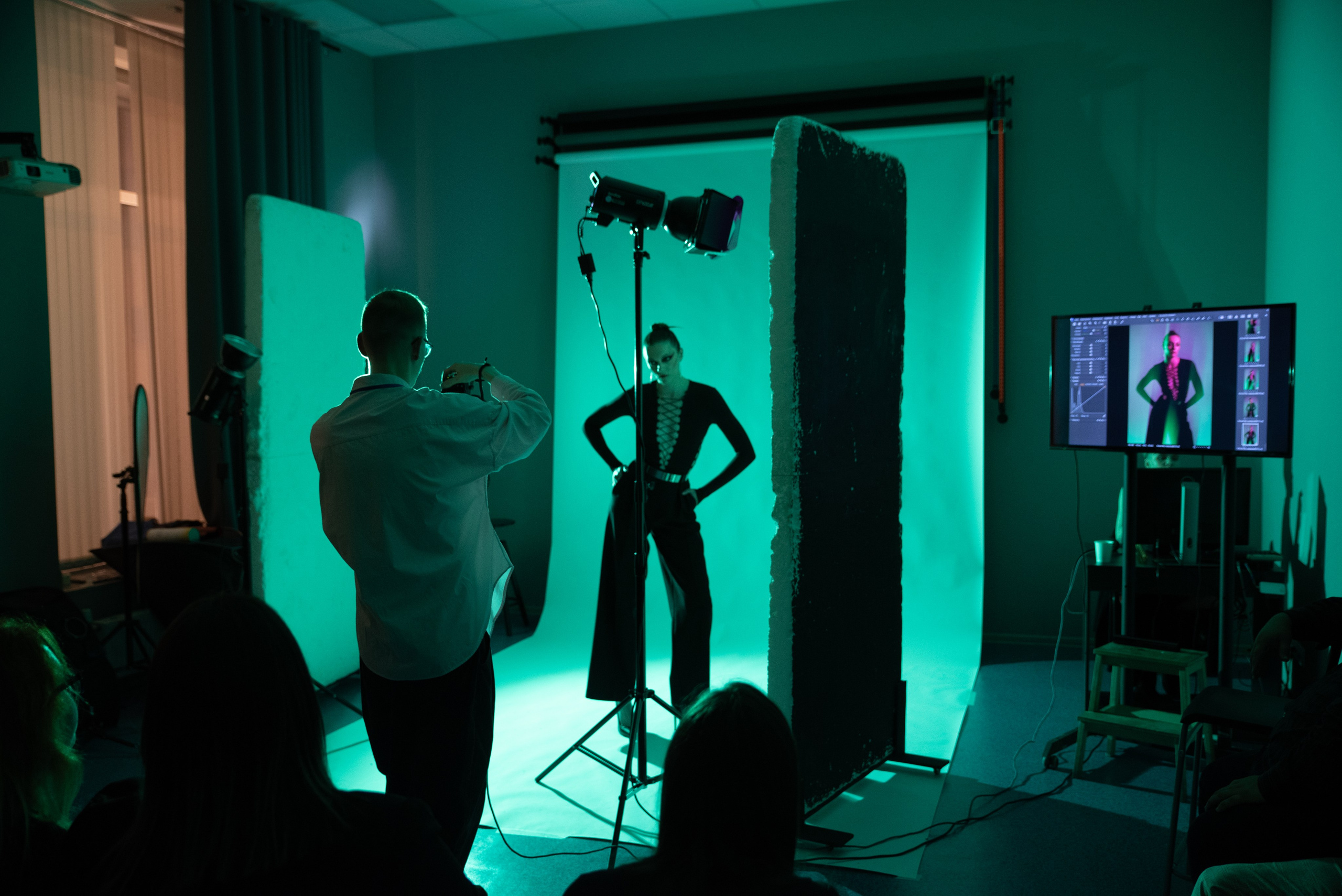 Фотограф снимает модель в студии, зелёный свет, изображение модели повторяется на мониторе сбоку.