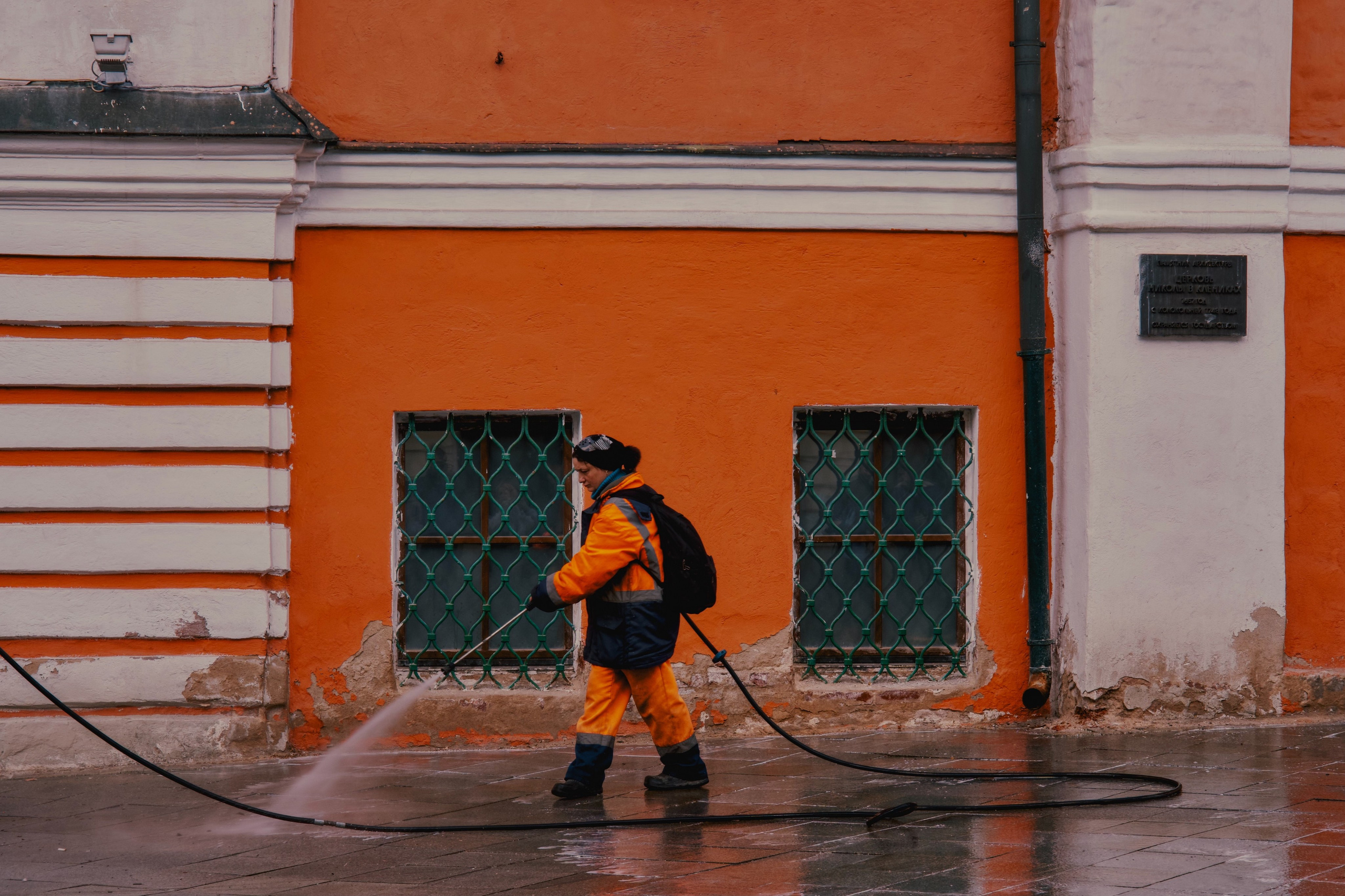 женщина в оранжевой форме поливает улицу на Маросеке