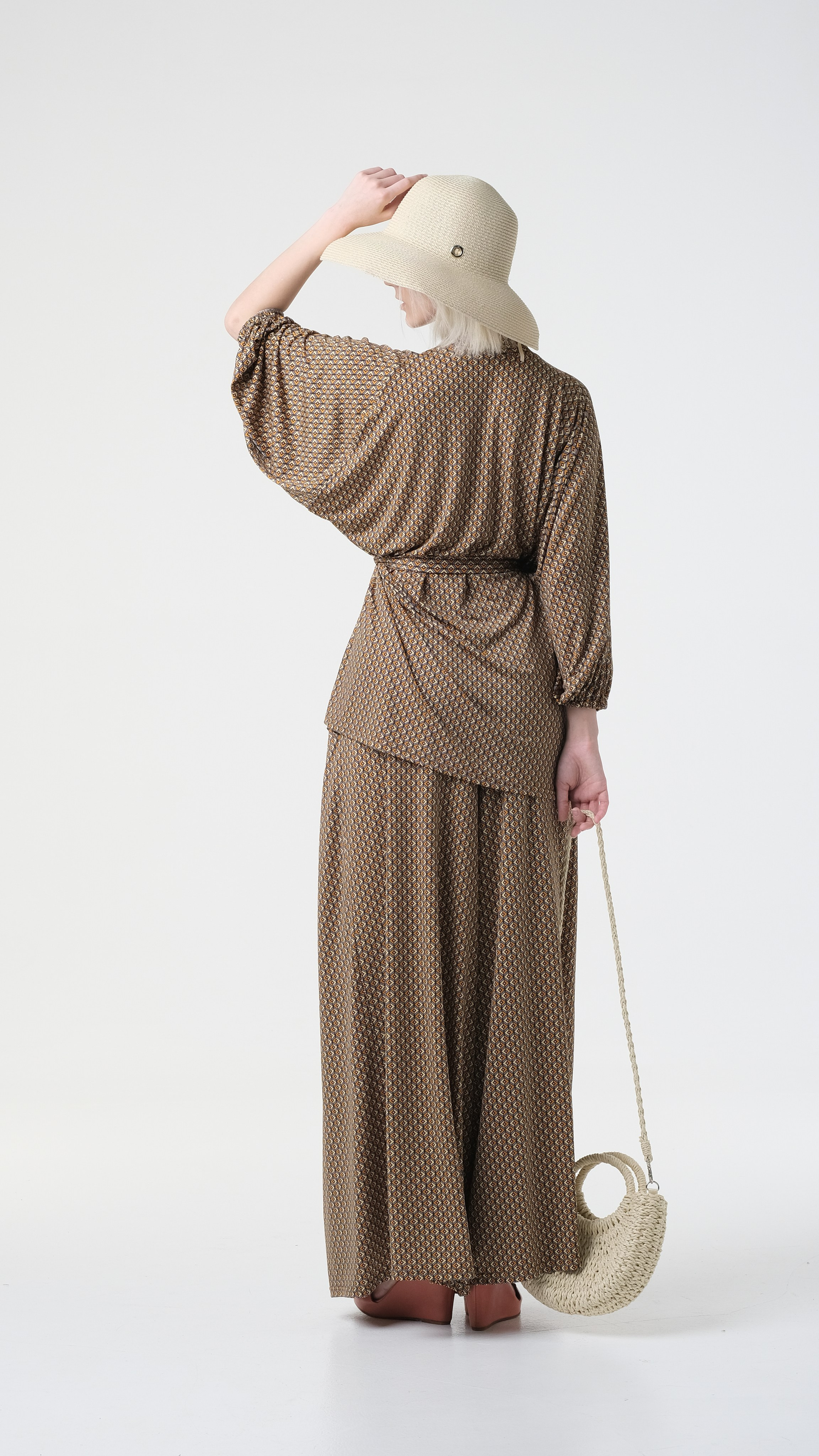 Фото на циклораме со спины. Модель в головном уборе и с сумкой в темном костюме.