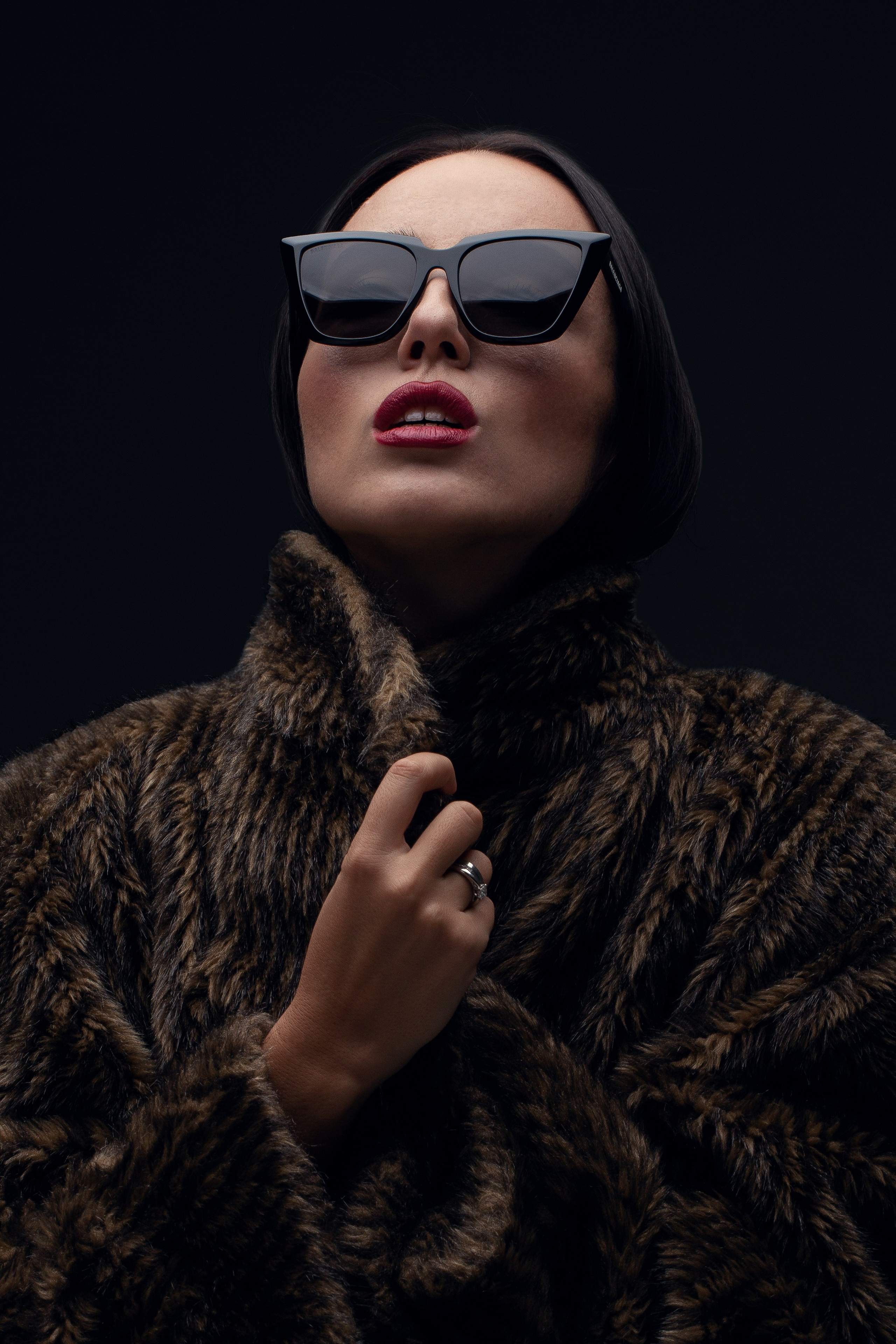 Стильный портрет женщины в леопардовом платке и меховой шубе, держащей солнцезащитные очки. Элегантный образ с ярким макияжем. Гламурный портрет: женщина в стиле ретро, сочетающем животный принт и роскошную меховую шубу. Фотография передает атмосферу шика и уверенности.