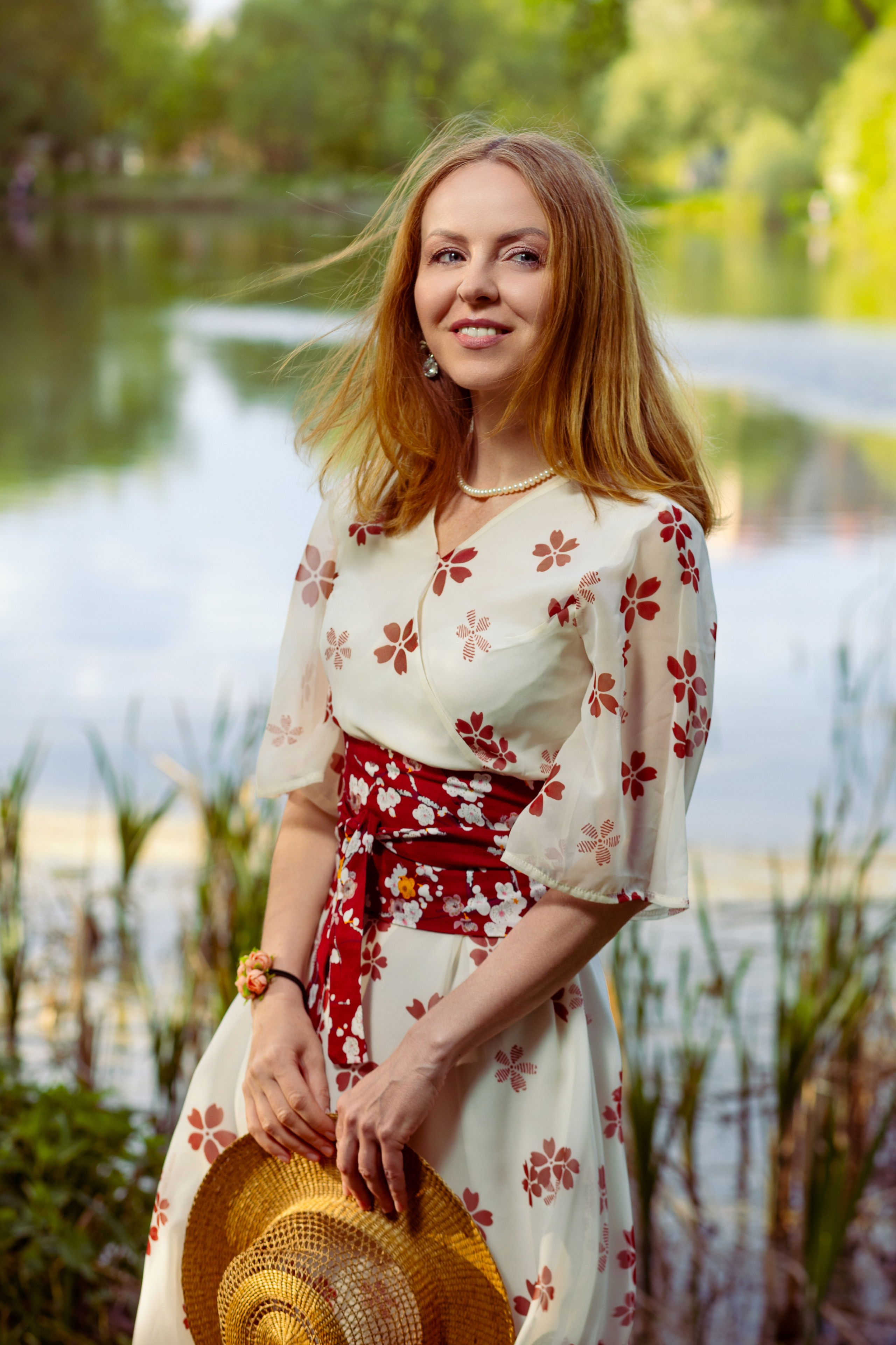 Девушка в красивом белом платье с цветами держит соломенную шляпку на фоне камышей