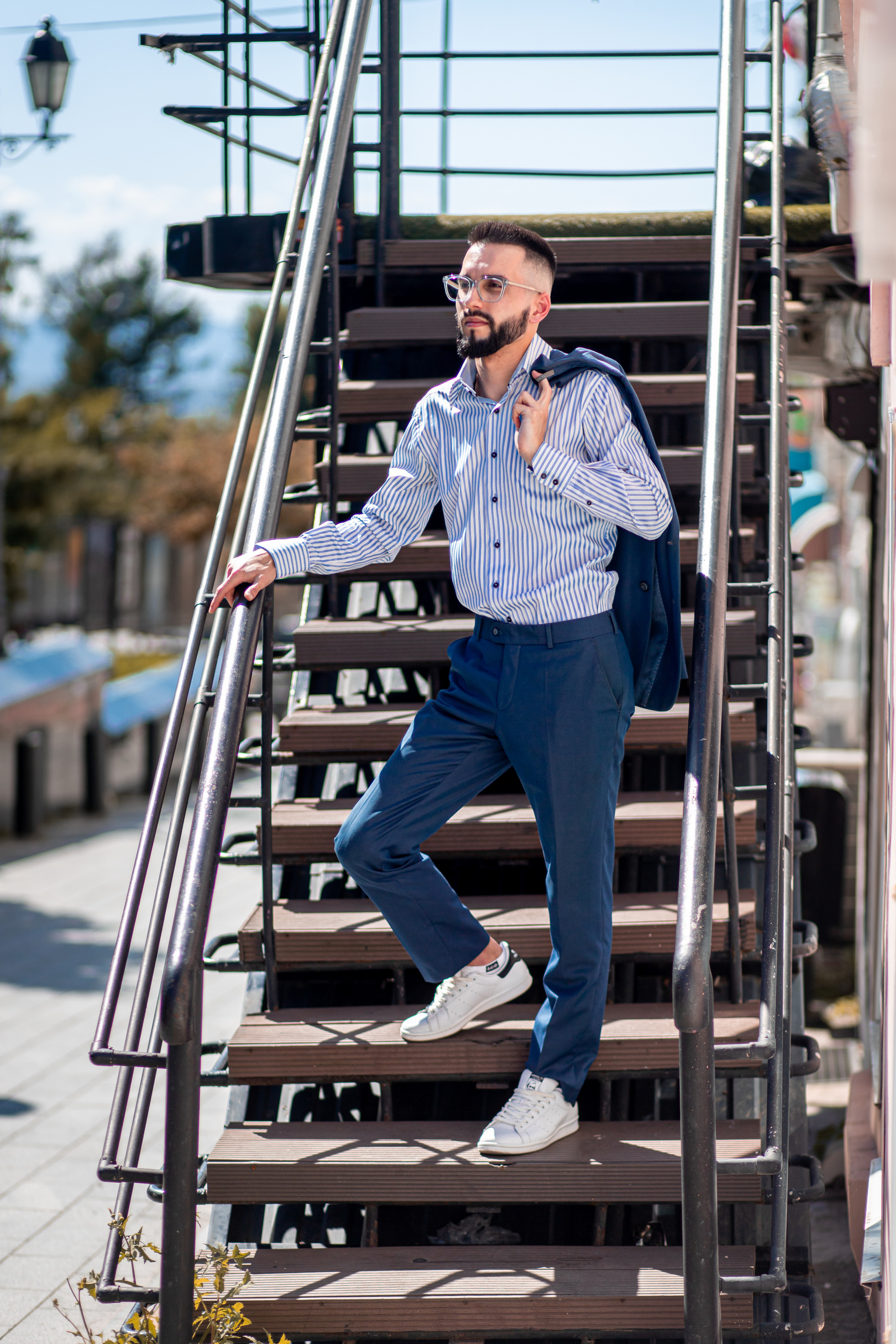 Мужчина в очках с пиджаком на плече стоит на лестнице смотрит в даль