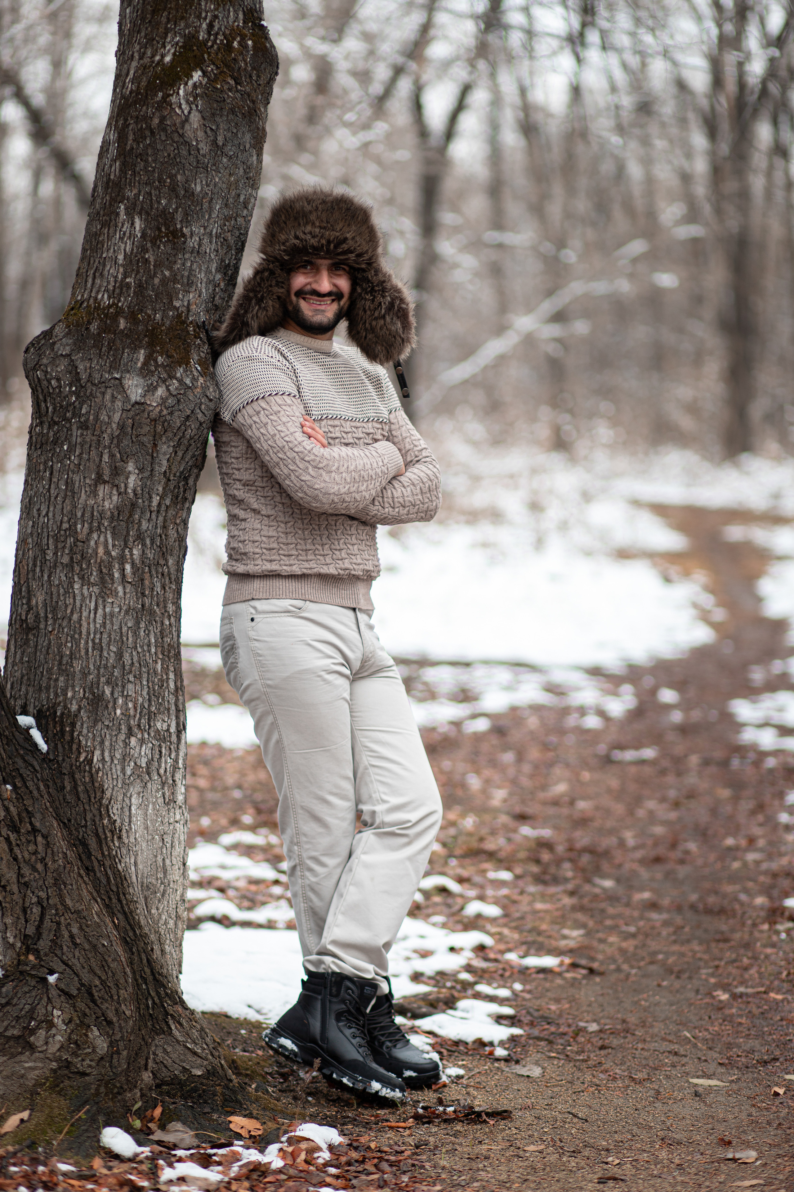 Мужчина стоит у дерева в шапке ушанке зимой улыбается Пограничный