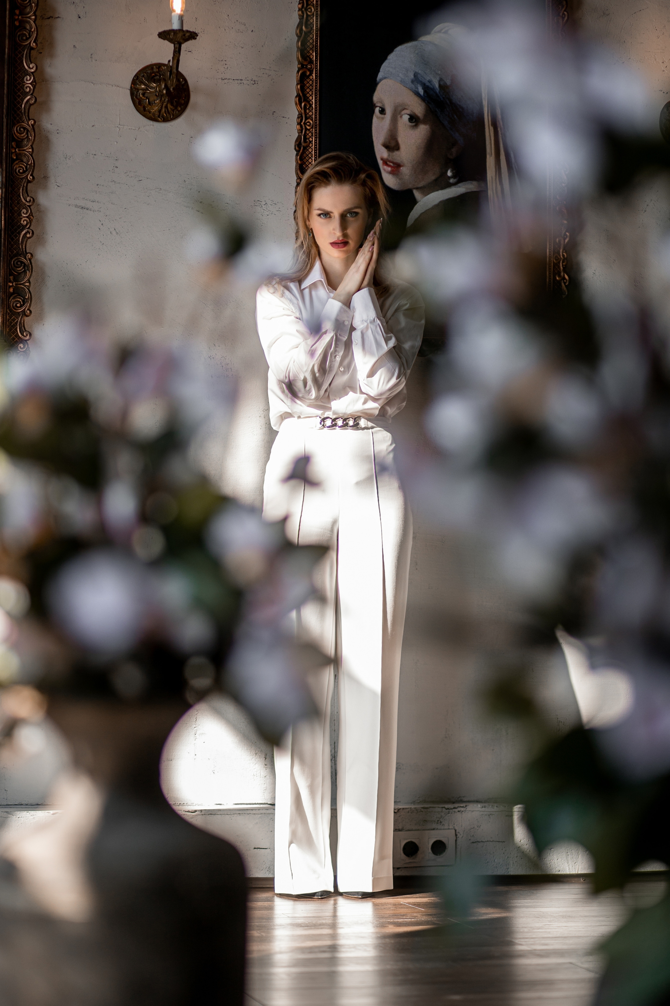 Девушка в белом сквозь цветы на фоне картин в фотосестудии. Бизнес фотосессия