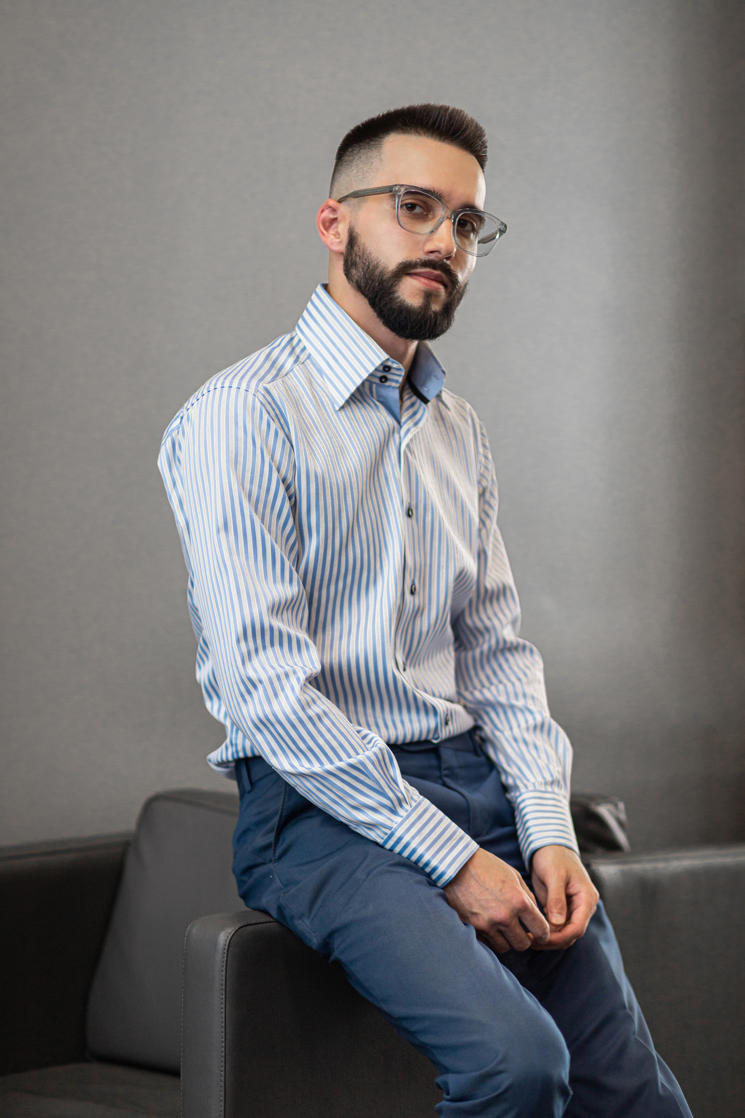 Мужчина в офисе в очках  сидит на ручке кресла деловая фотография