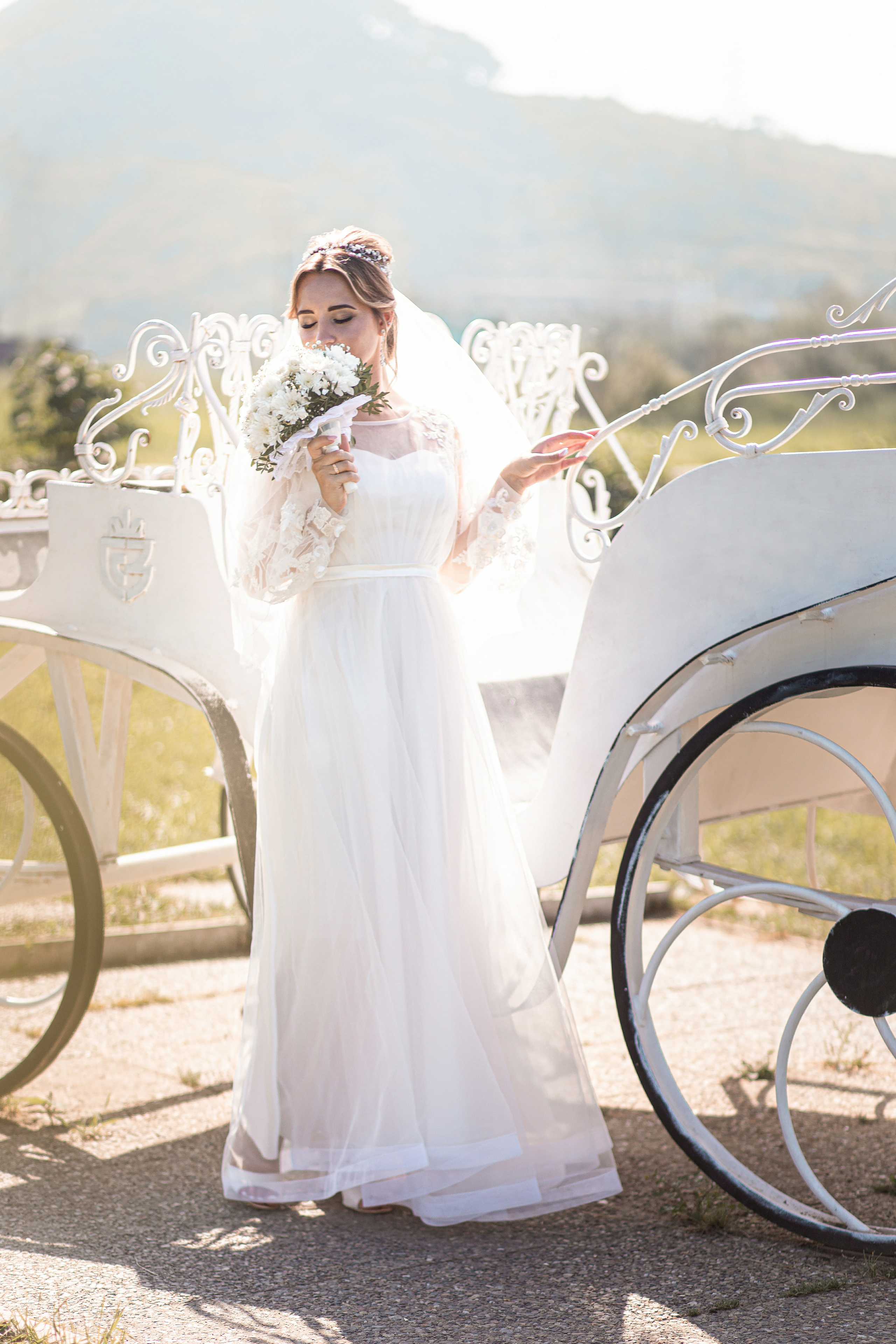 Невеста стоит около кареты на фоне гор в Славянке