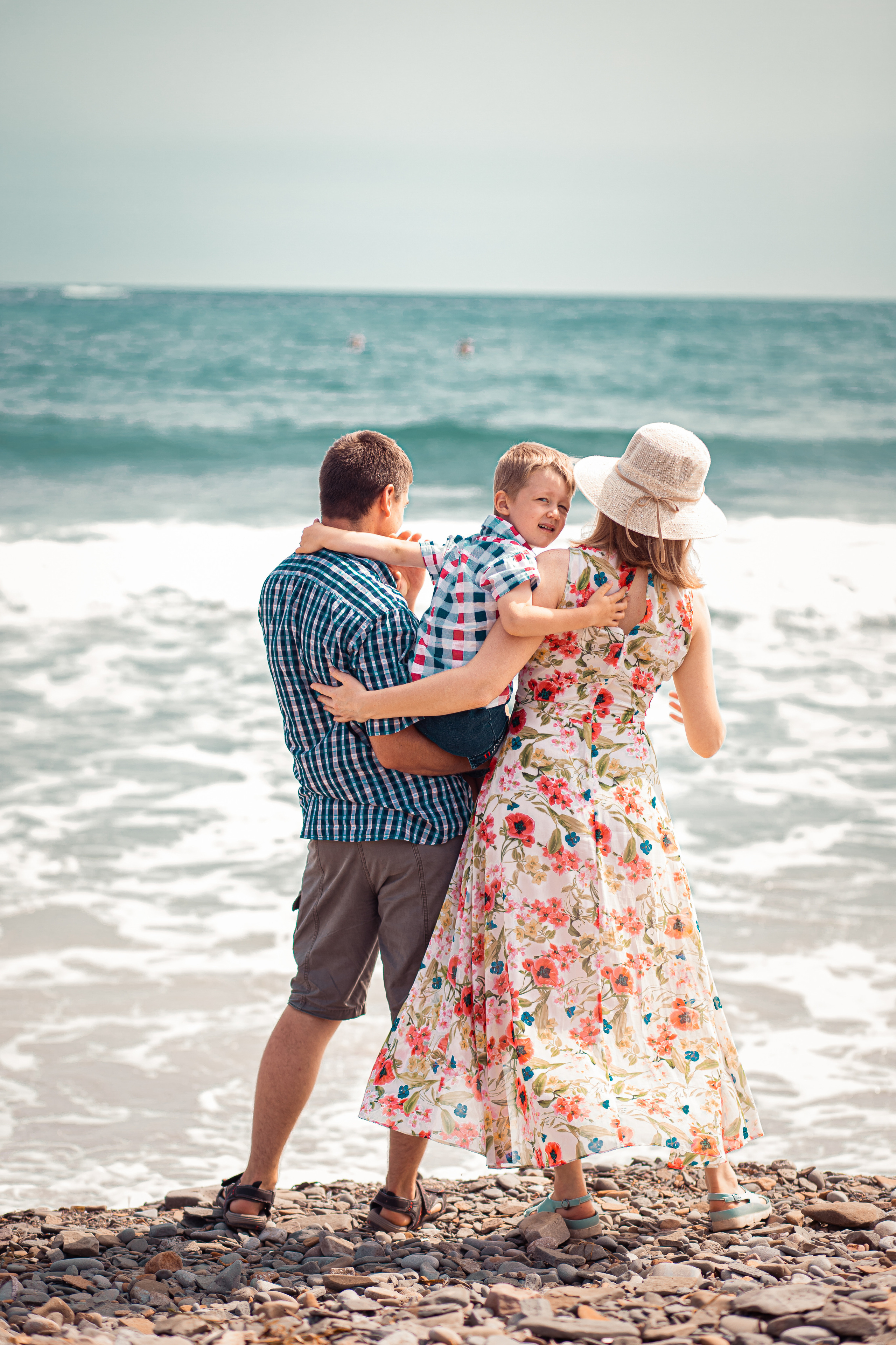 Ребёнок смотрит в камеру, когда родители его держат на руках на фоне моря на Острове Русский во Владивостоке