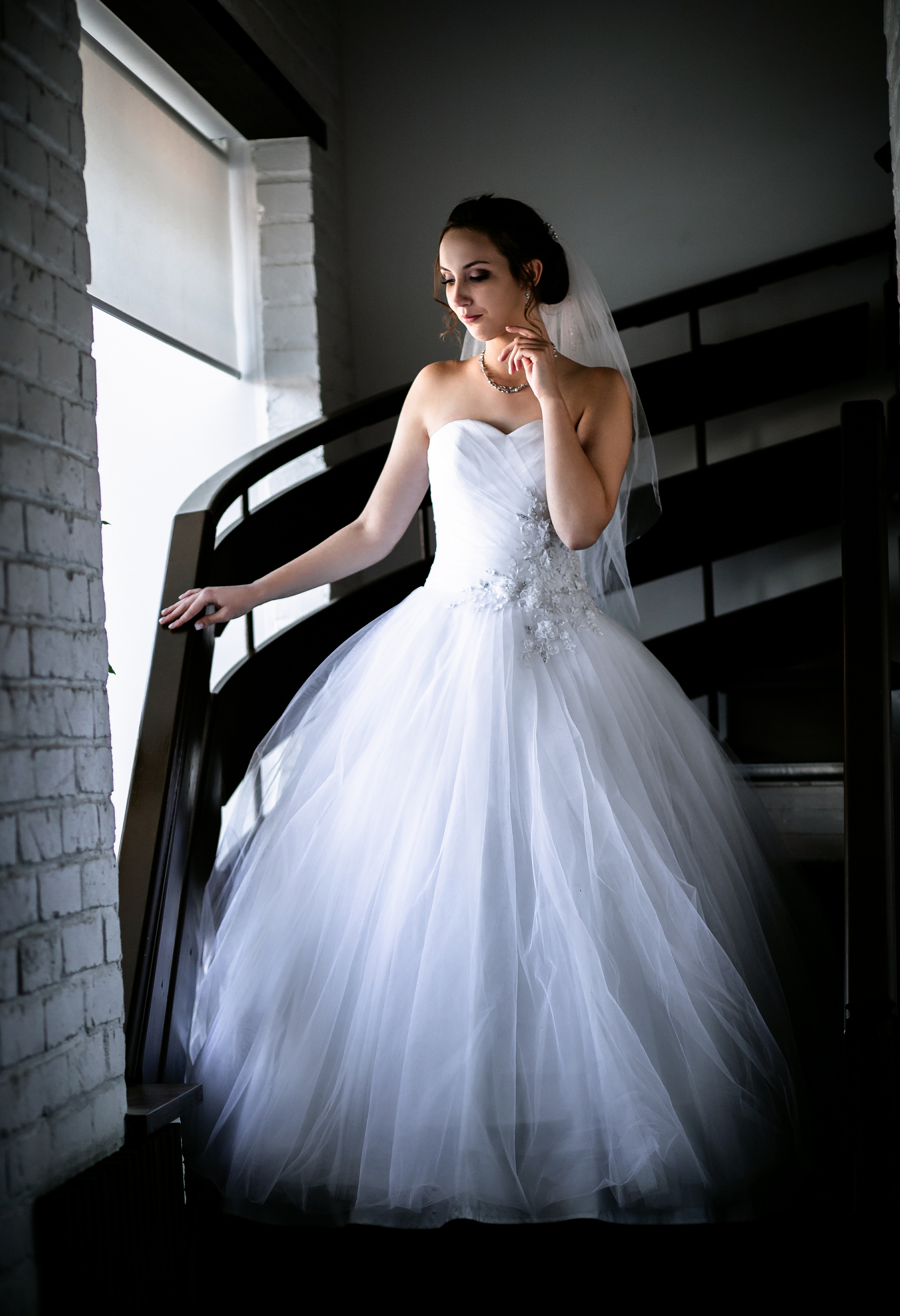 Задумчивая невеста спускается по лестнице смотря в окно держась за поручень в отеле Свадебная фотосессия в Спасске