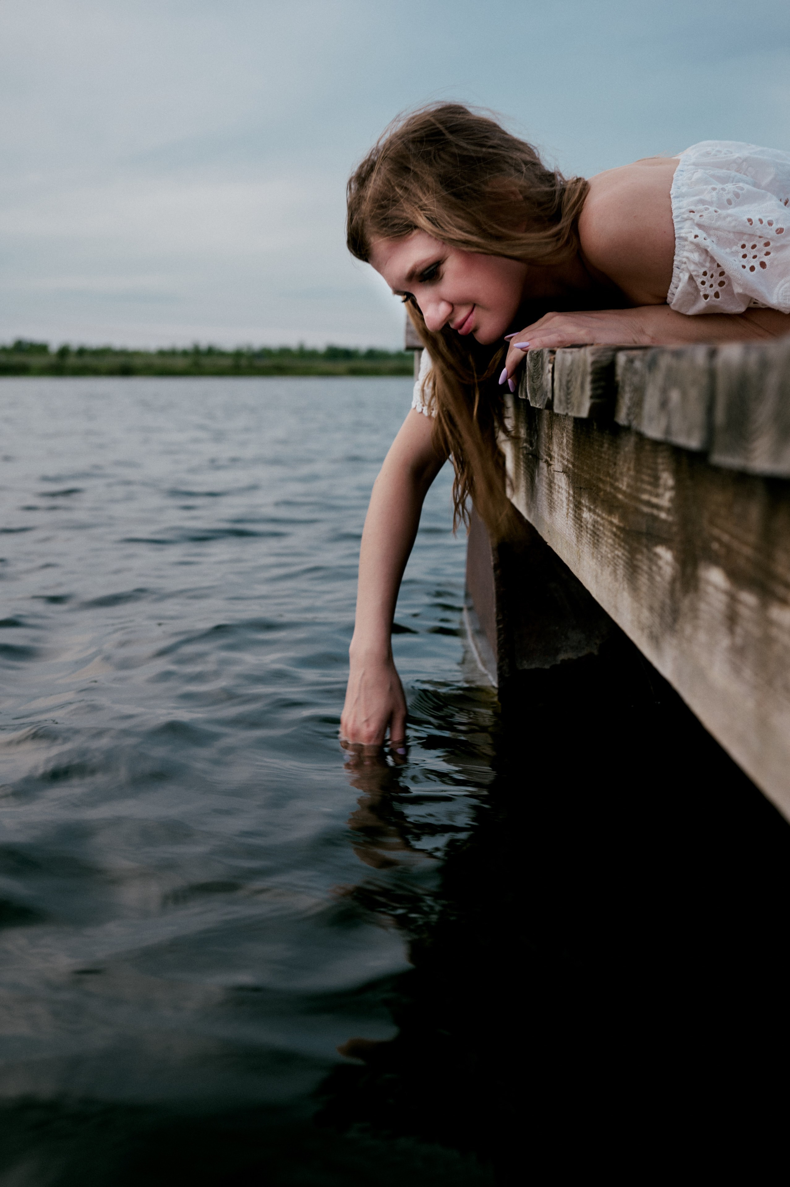 Евгения лежит на деревянном пирсе, опустив руку в воду.