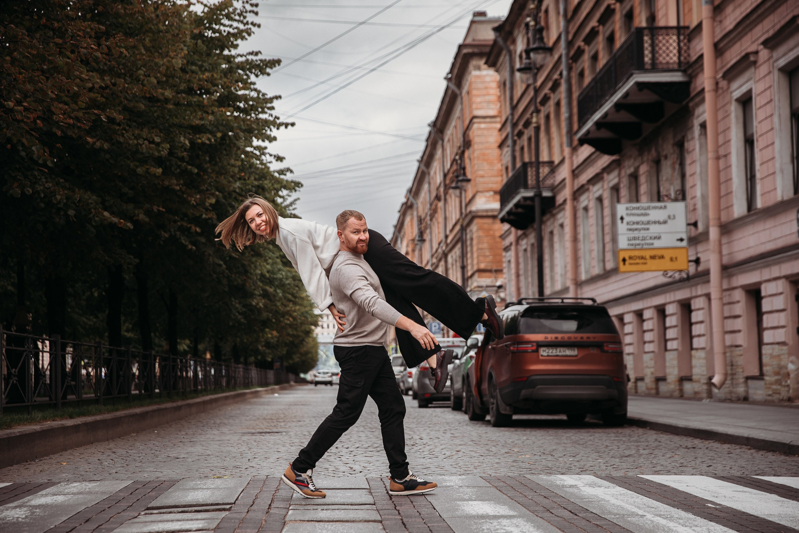 Молодой человек несет на плече девушку через пешеходный переход в Петербурге
