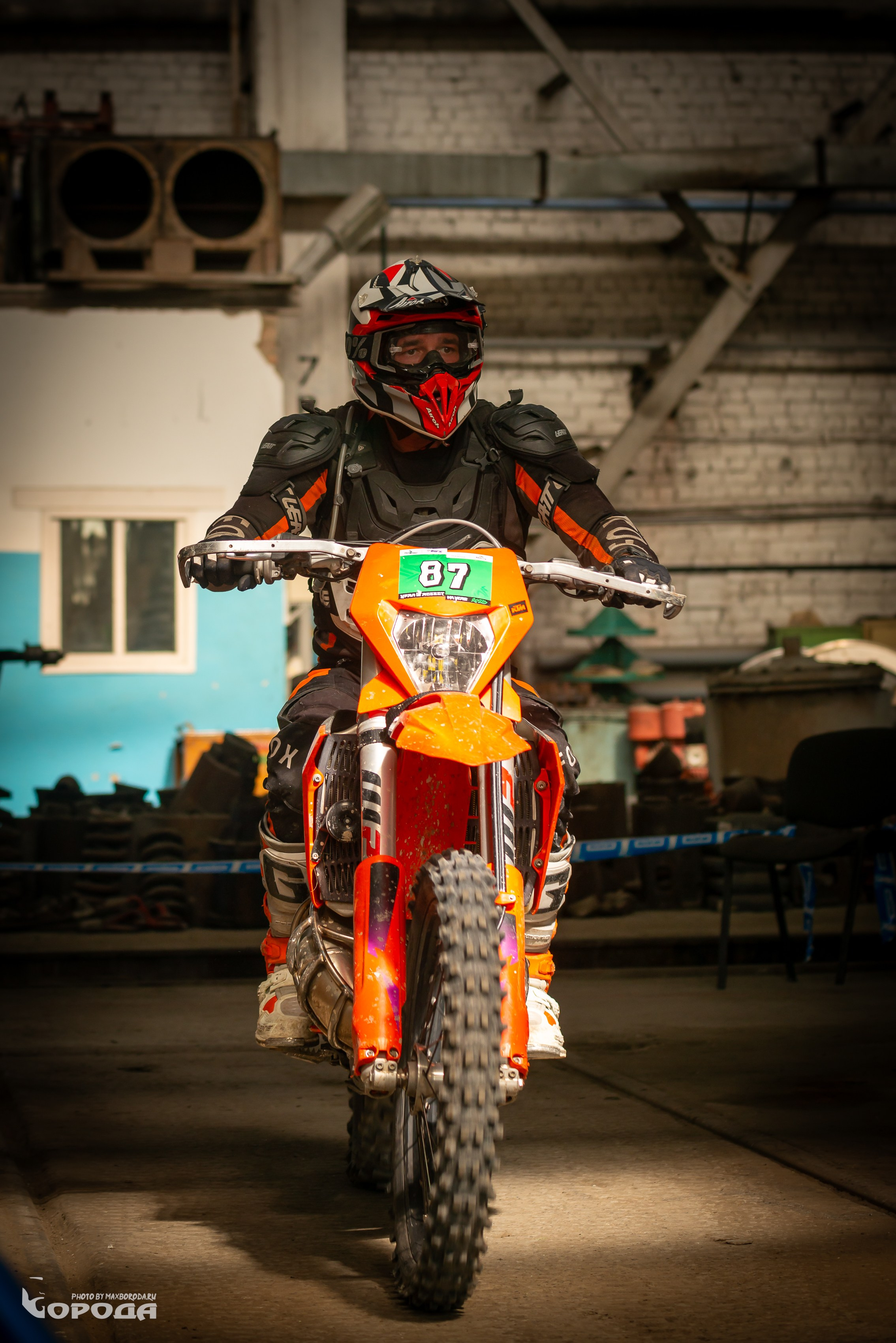 Гонщик с номером 87 на оранжевом эндуро в заброшенном промышленном здании.