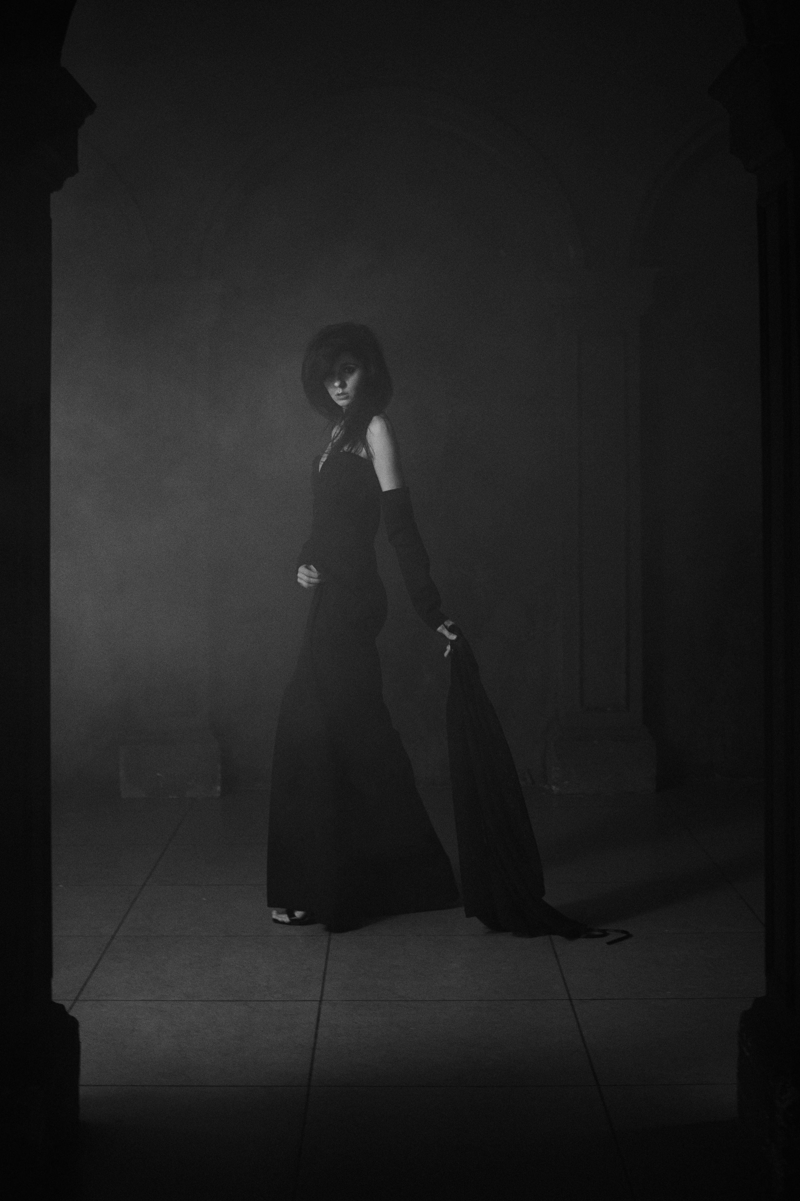 Черно-белая фотография девушки, бредущей медленно между колонн в дымке, волоча за собой черную шаль
