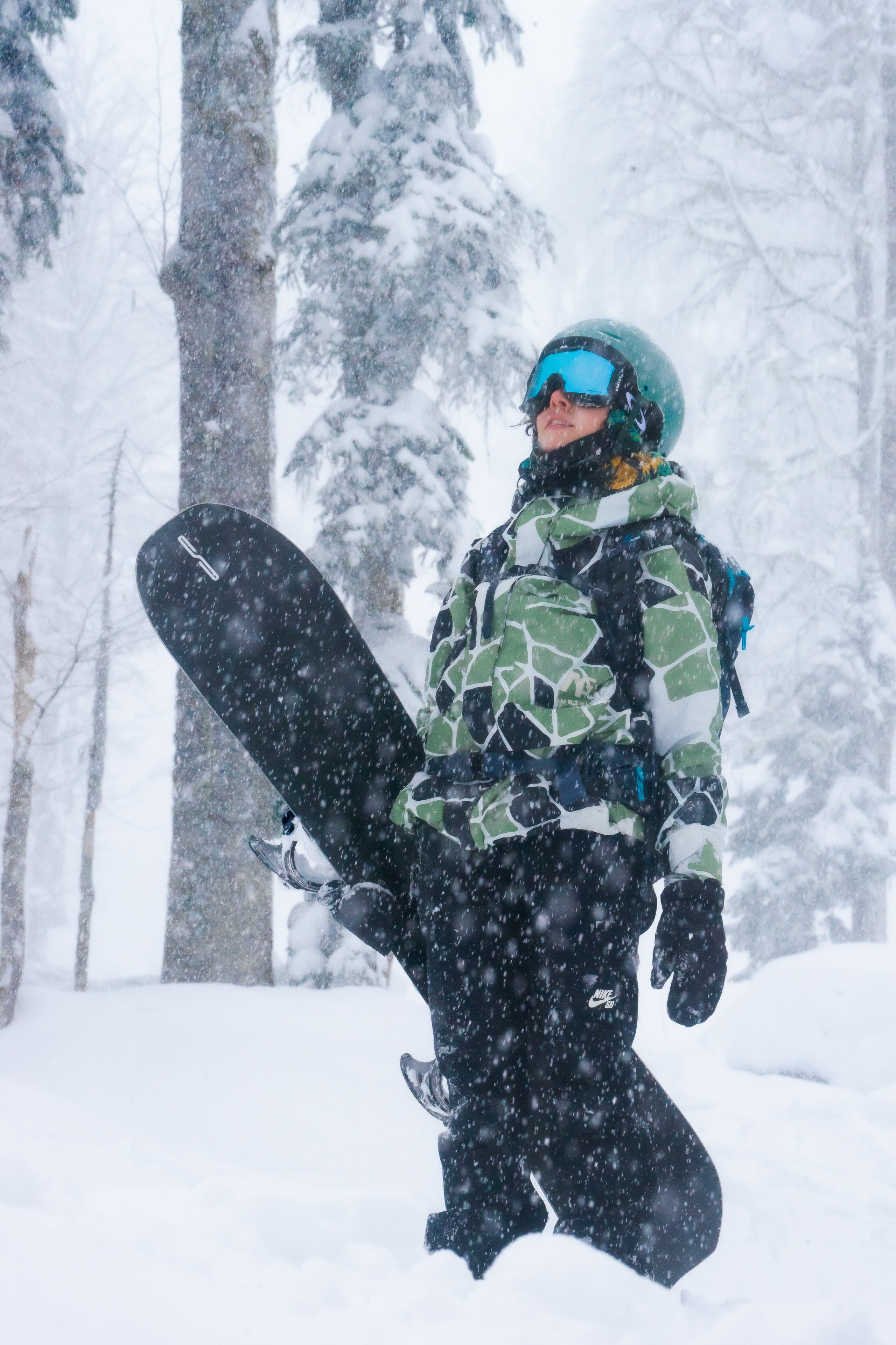 девушка со сноубордом стоит в горном лесу во время сильного снегопада