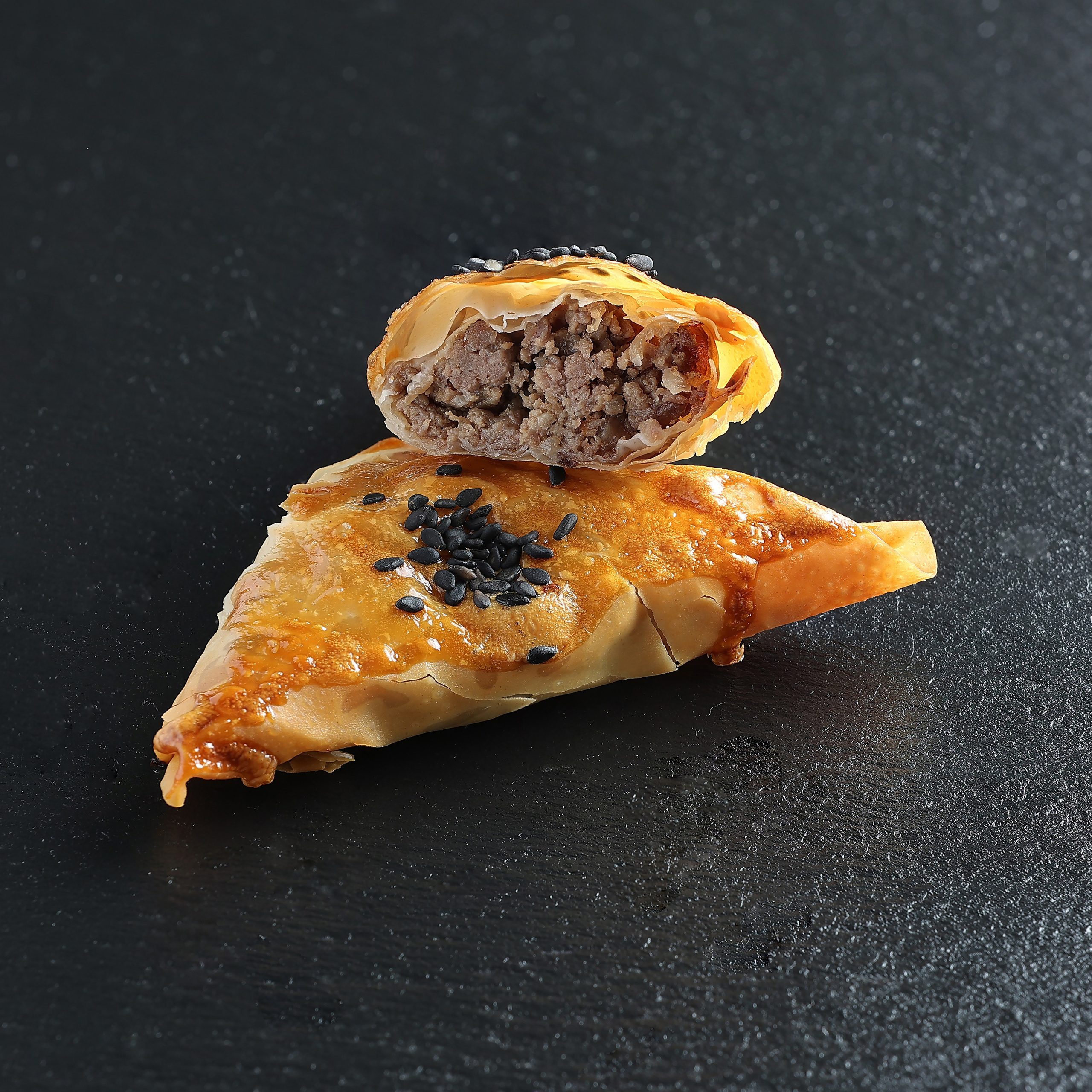 Два круассана с мясной начинкой на тёмном фоне: один целый с кунжутом, второй — в разрезе, видна мясная начинка.