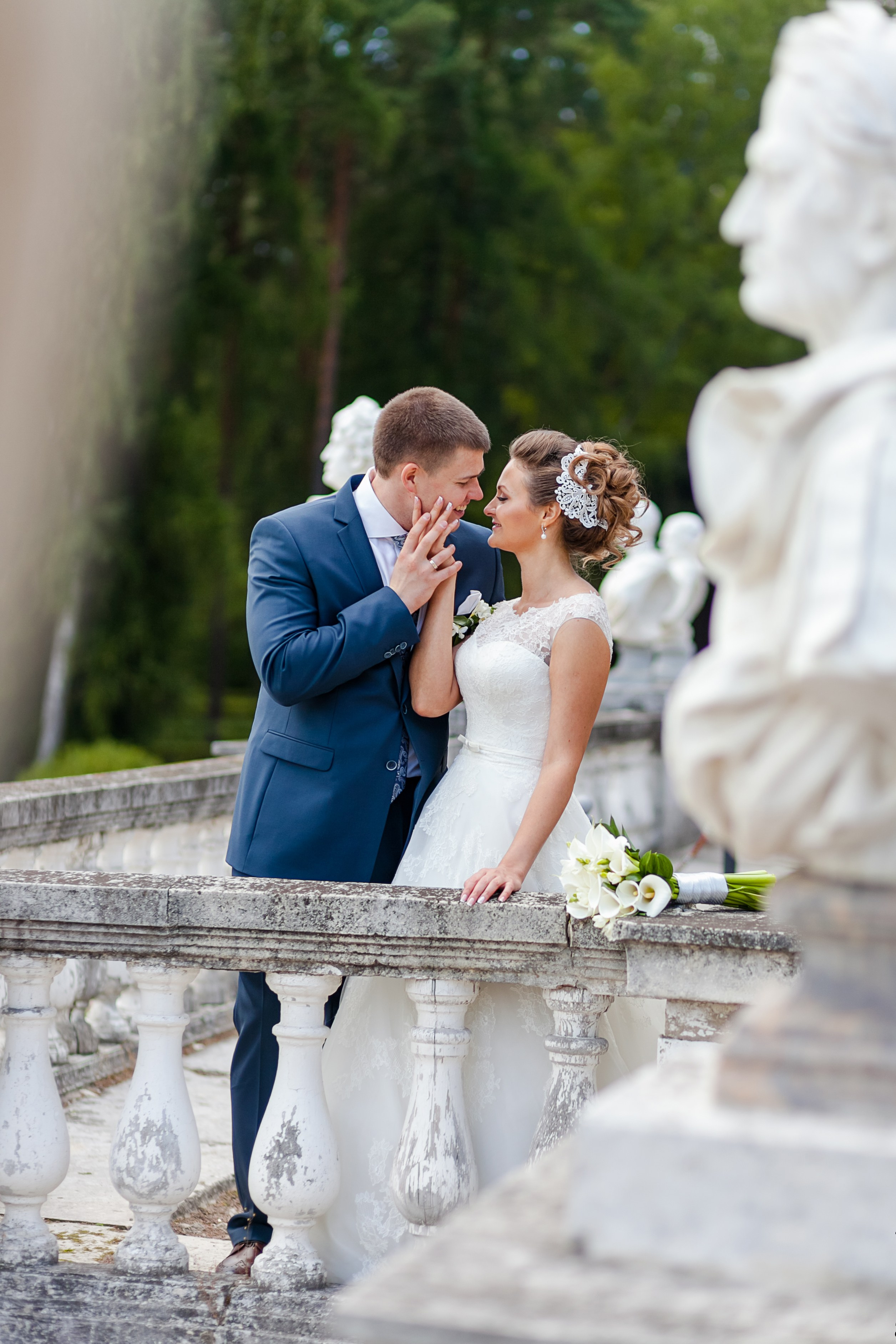 Свадебный поцелуй в парке на фоне скульптур