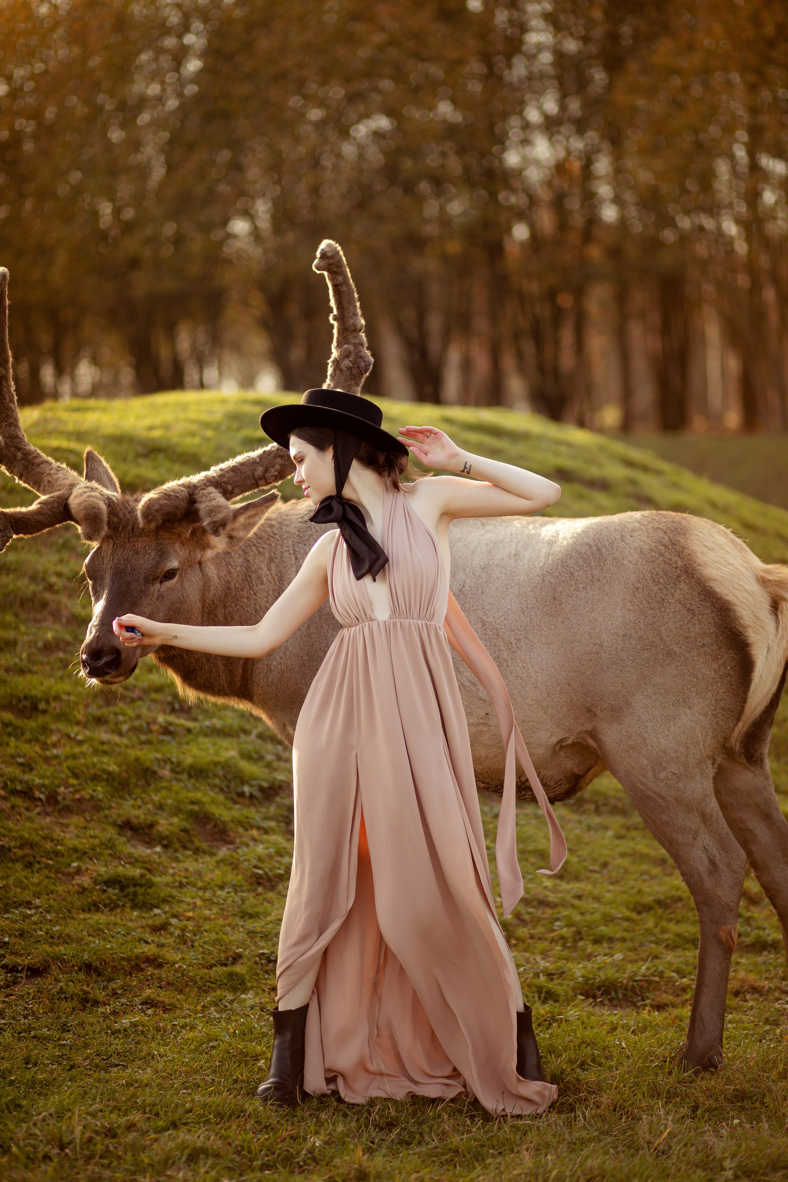 Девушка стоит во весь рост и гладит оленя.