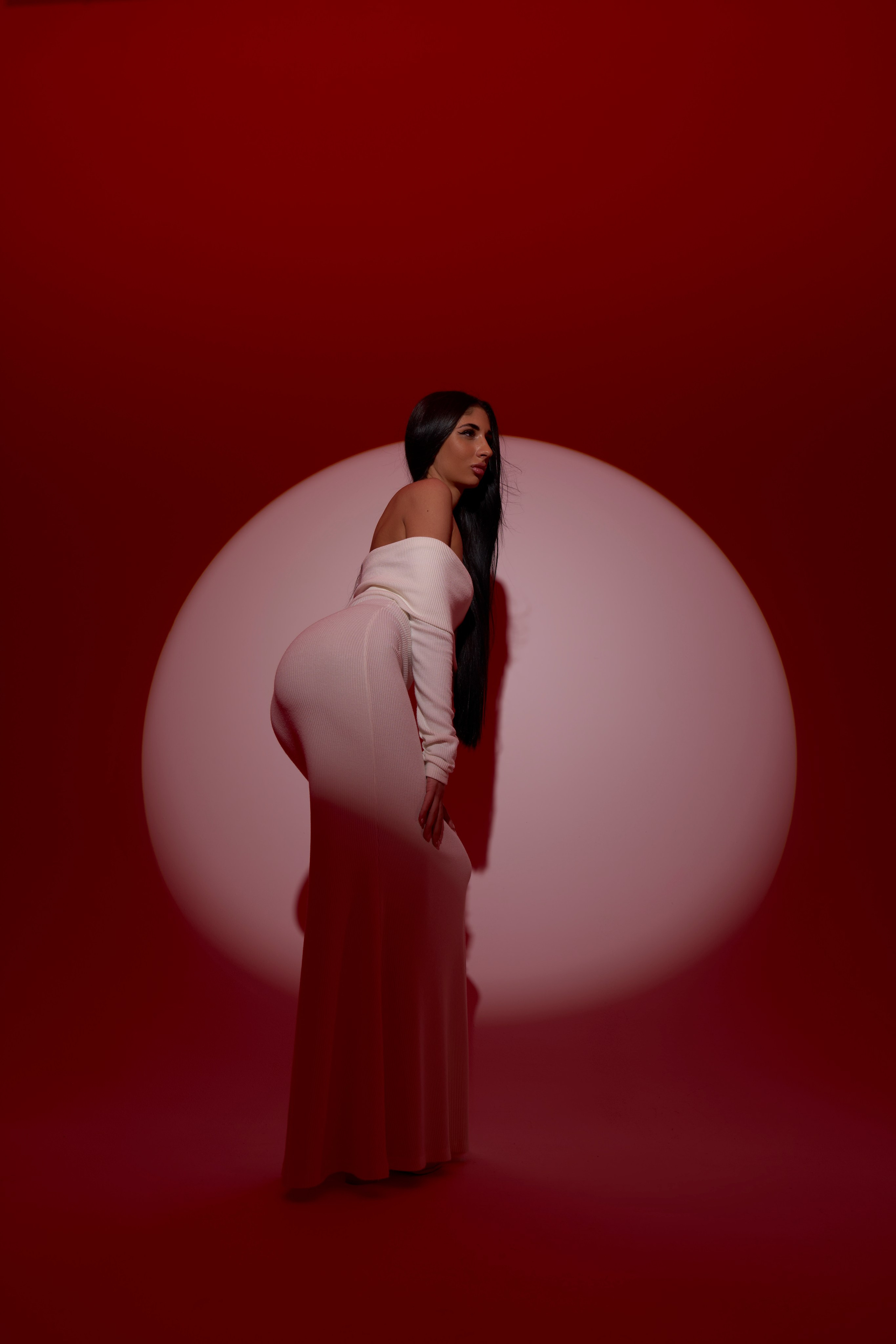 Завершающий кадр фотосессии в Москве: модель в белом платье стоит на фоне светового круга, элегантная поза