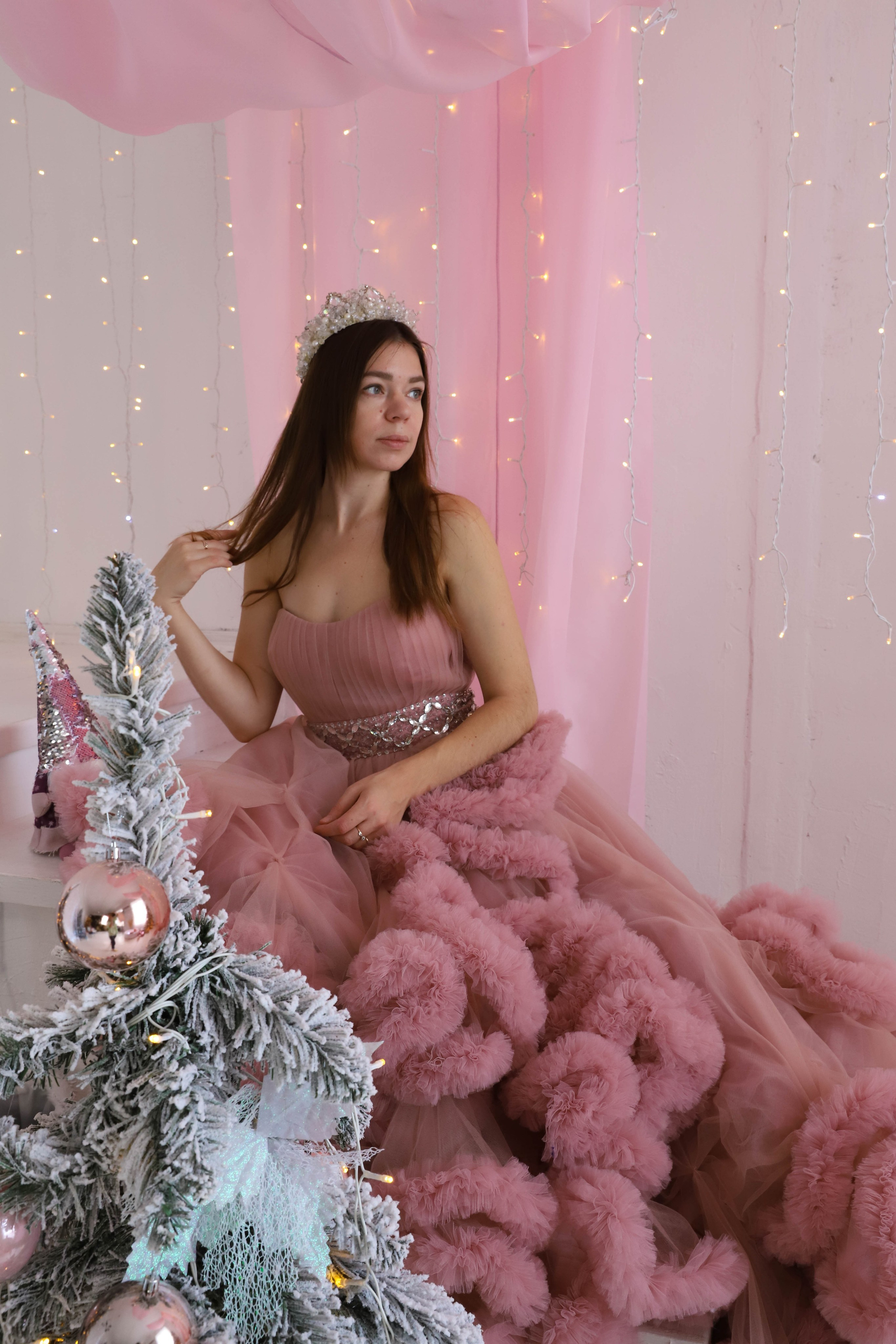 Красивая девушка в розовом бальном платье позирует на заднем плане,а на переднем плане новогодняя елка