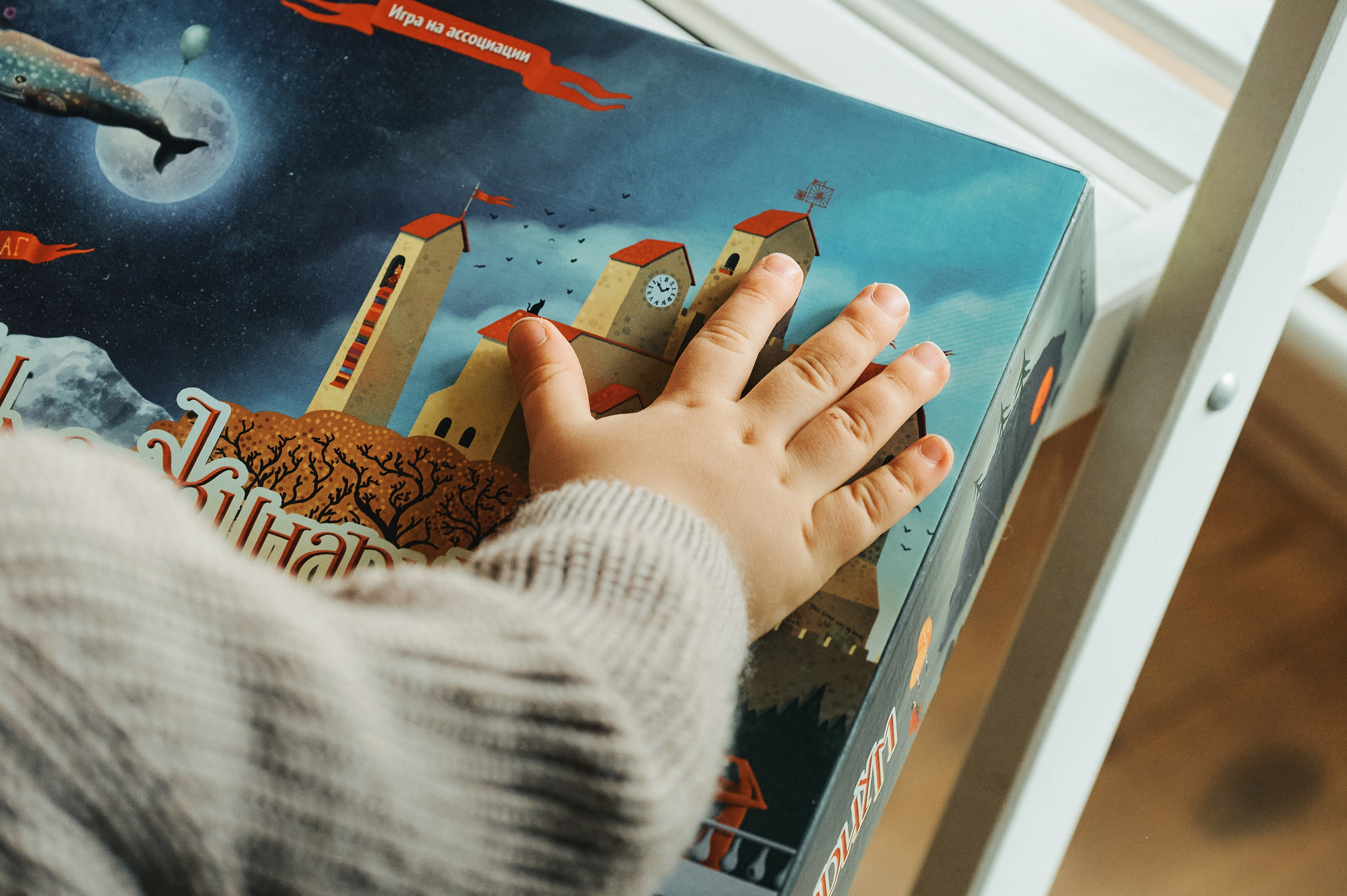 Рука ребёнка на коробке настольной игры с яркой иллюстрацией замка.