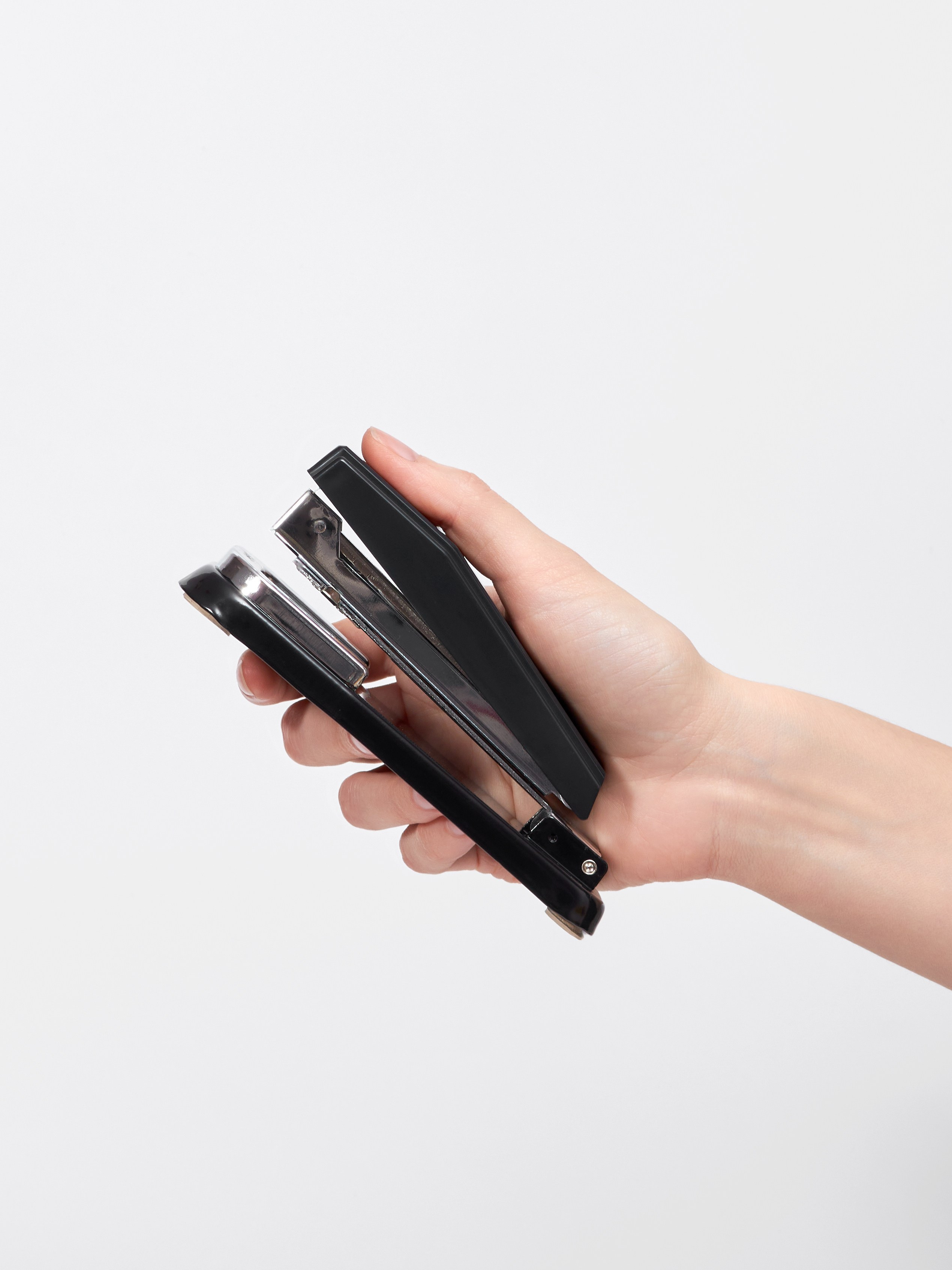 Предметная фотосъёмка черного канцелярского степлера в руках модели на белом фоне