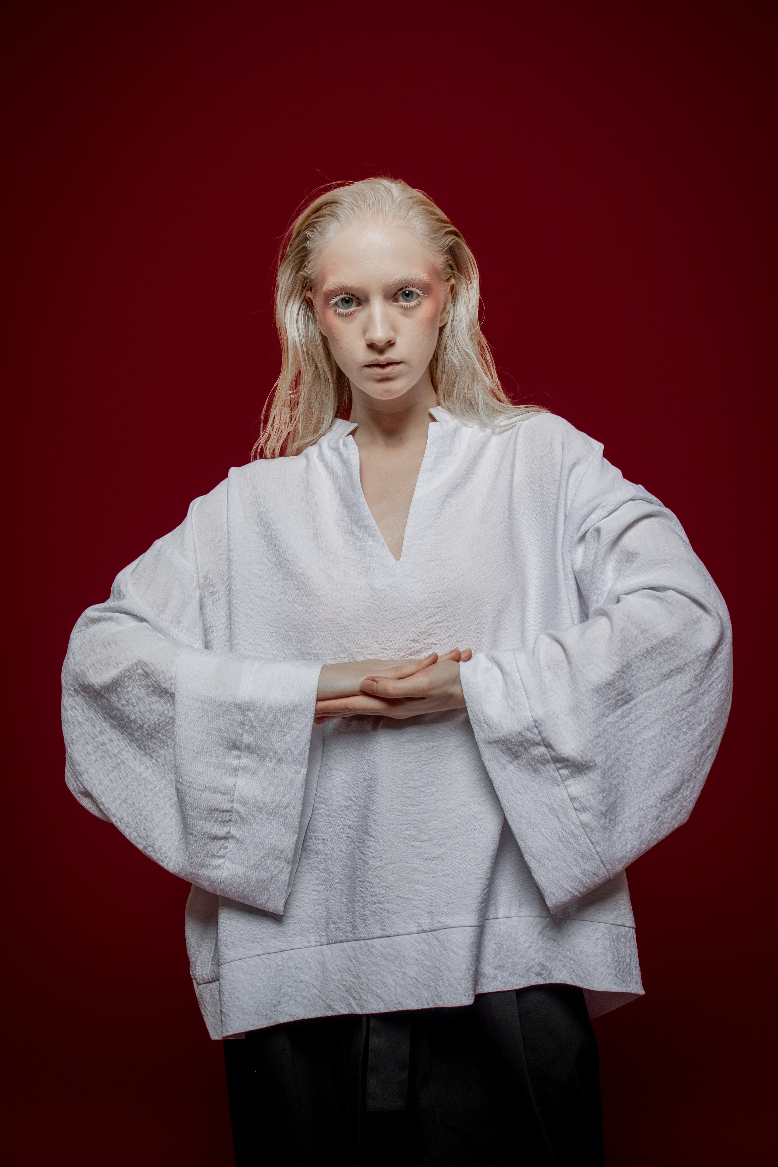 Девушка модель блондинка в белой кофте на красном фоне