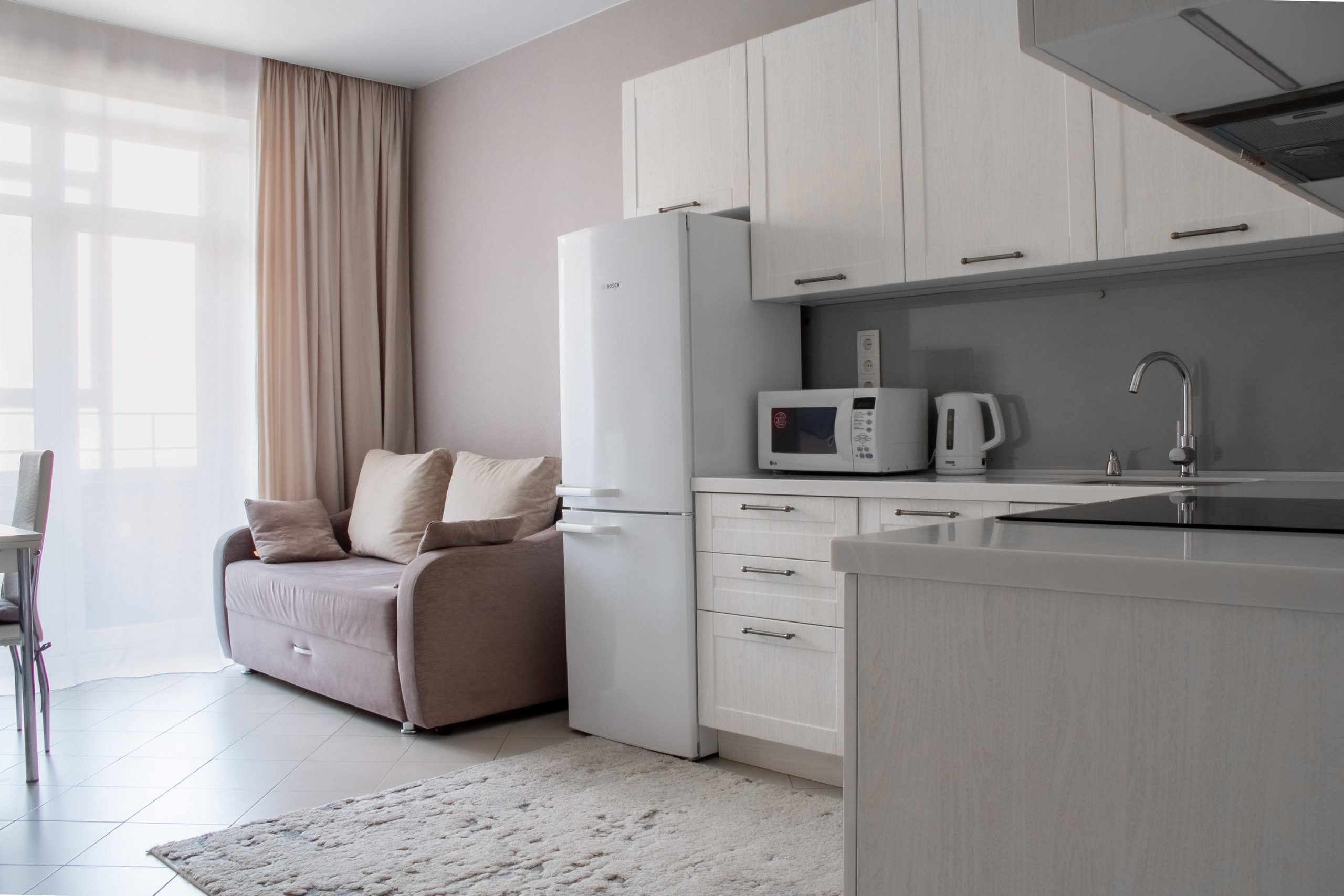 Большая, светлая кухня. Гарнитур в светлых тонах, есть раскладной диван, большое окно. 