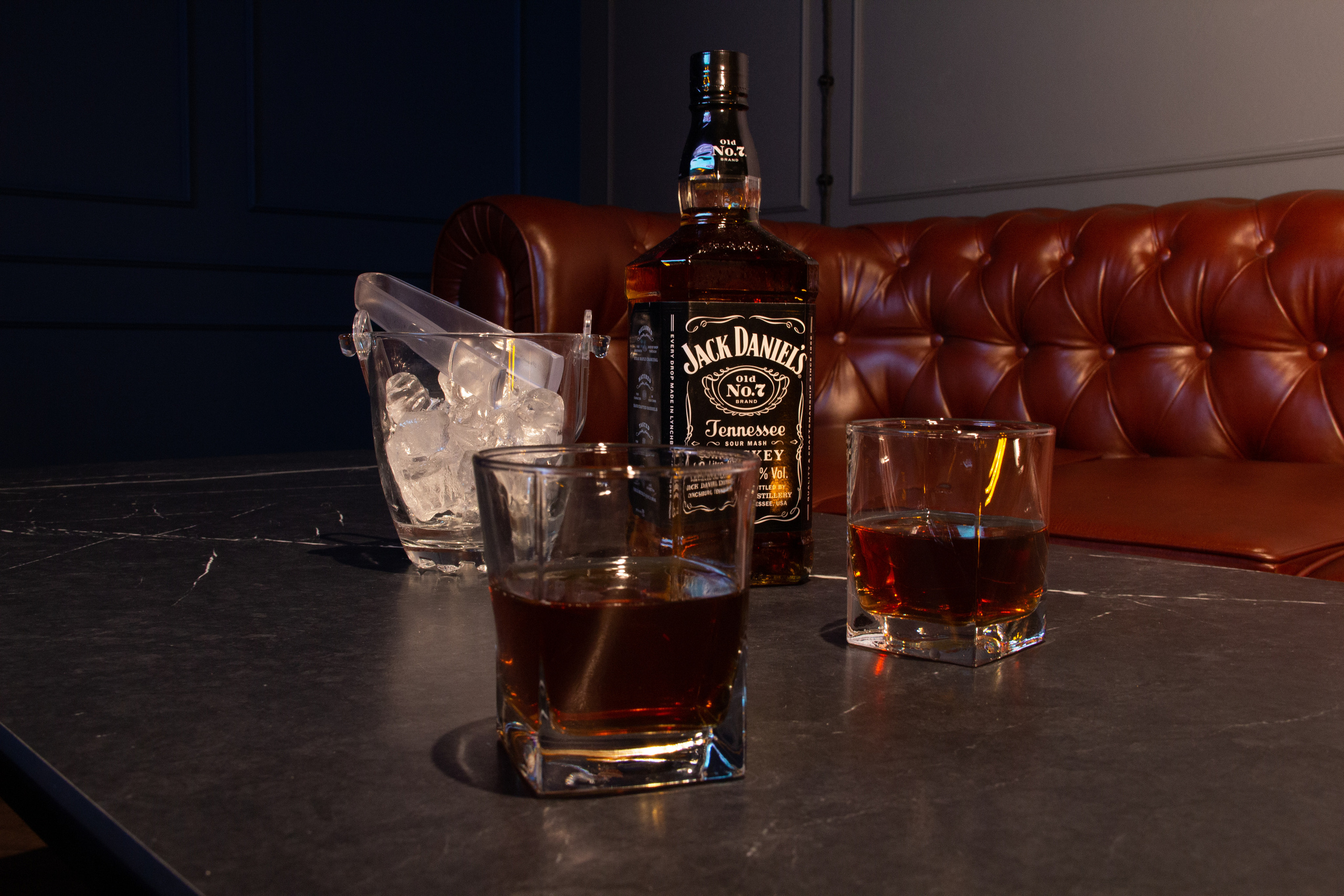 Большой кожаный диван, лофт стол и дорогой элитный алкоголь. Приглушенный свет.