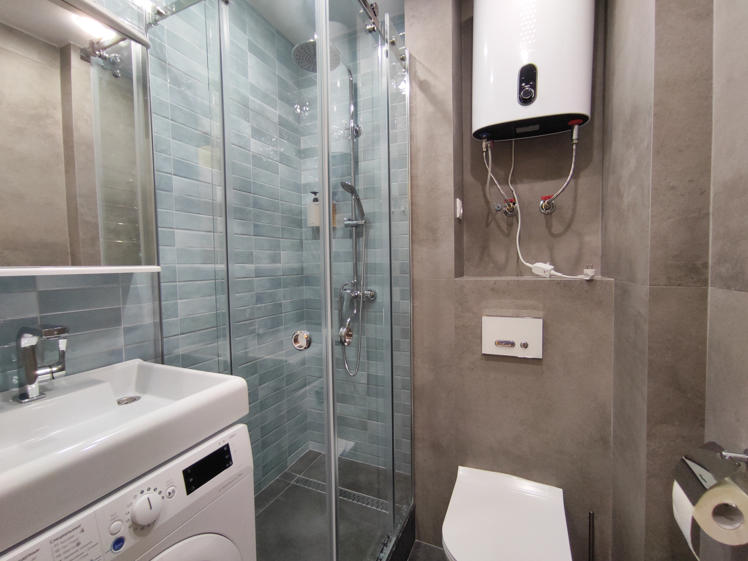 Стильная, светлая ванная комната с душевой кабиной. Имеется стиральная машинка автомат и раковина.  