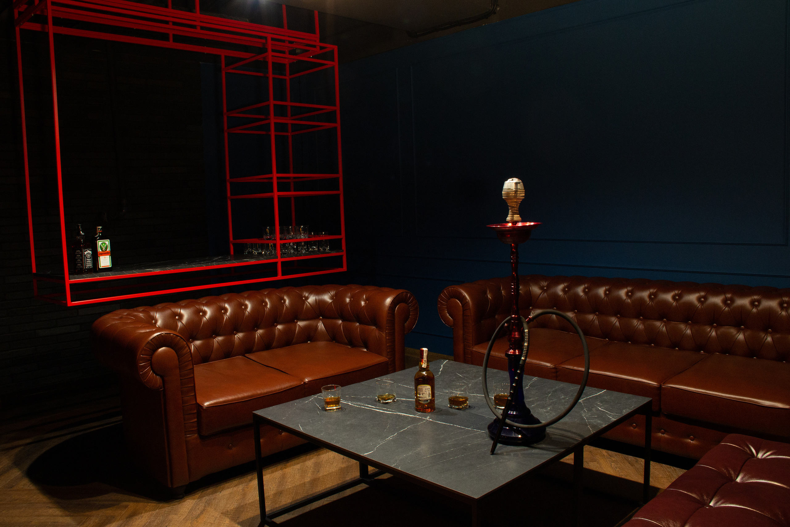 Большая комната отдыха с большими кожаным диваном и креслами. Стильный красный бар, интимная обстановка.