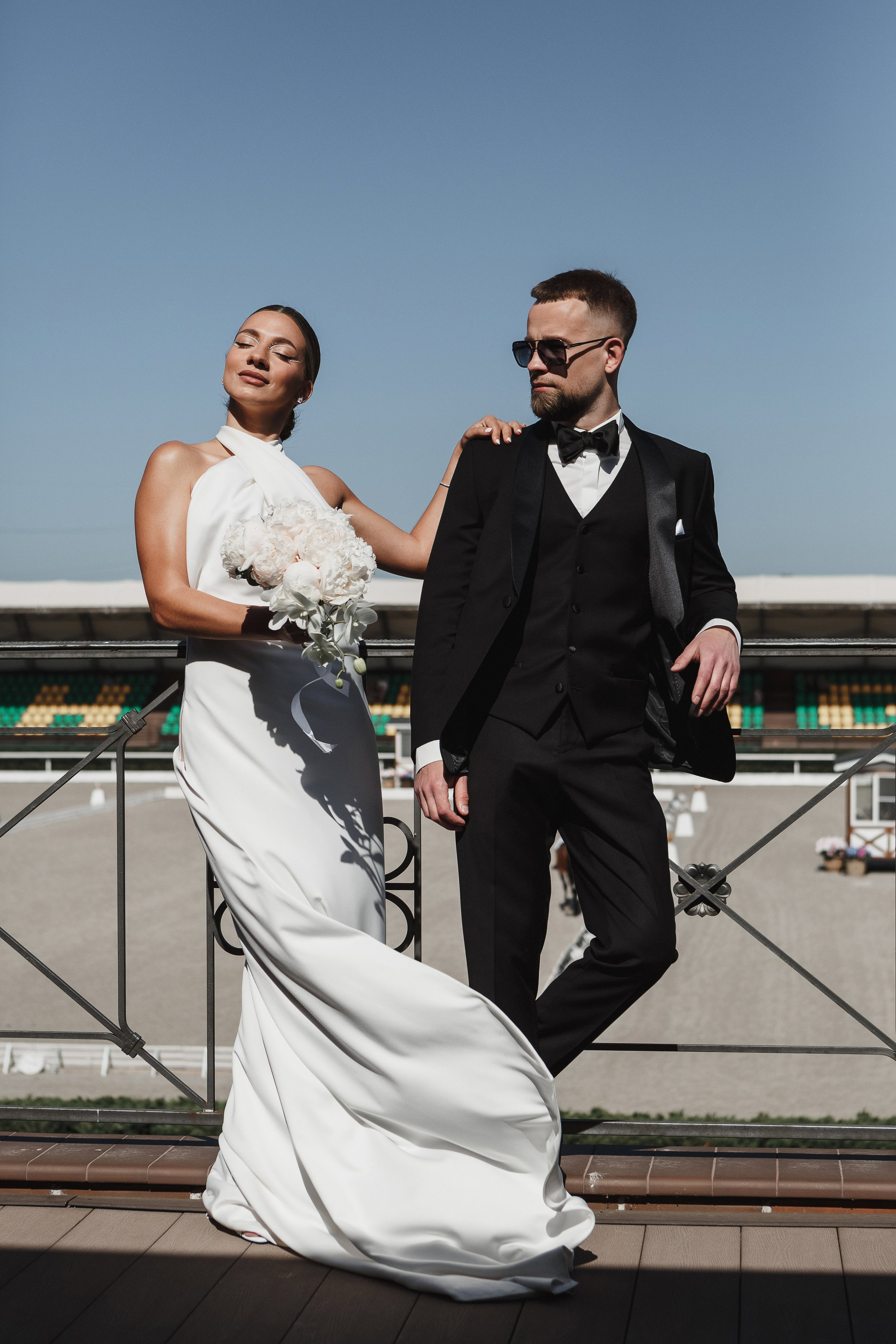 Невеста с букетом и жених в смокинге позируют на балконе Golden Horse в Таганроге, свадебный фотограф Антон Бакарюк