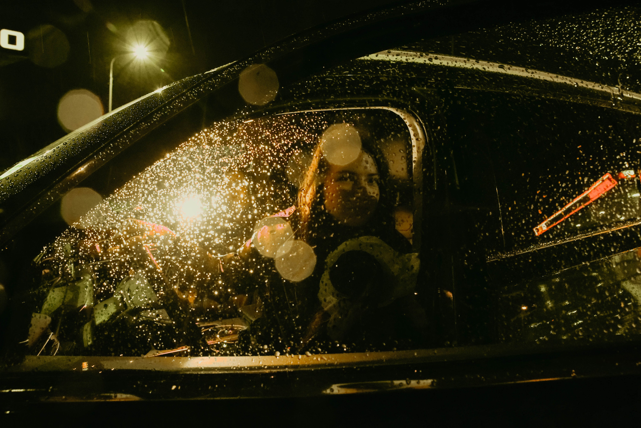 Фотосессия девушки ночью под дождем в машине на заправке через мокрое стекло