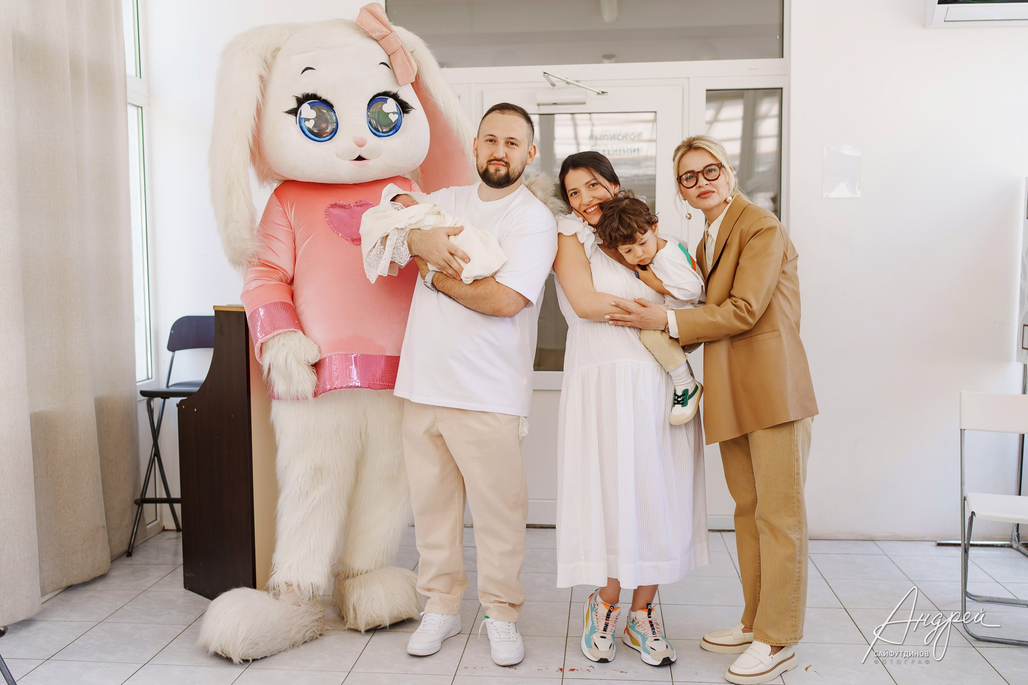 Молодые родители с новорожденной на фотозоне роддома ЦГБ в окружении гостей и ростовой куклы, Ростов-на-Дону, фотосъемка выписки